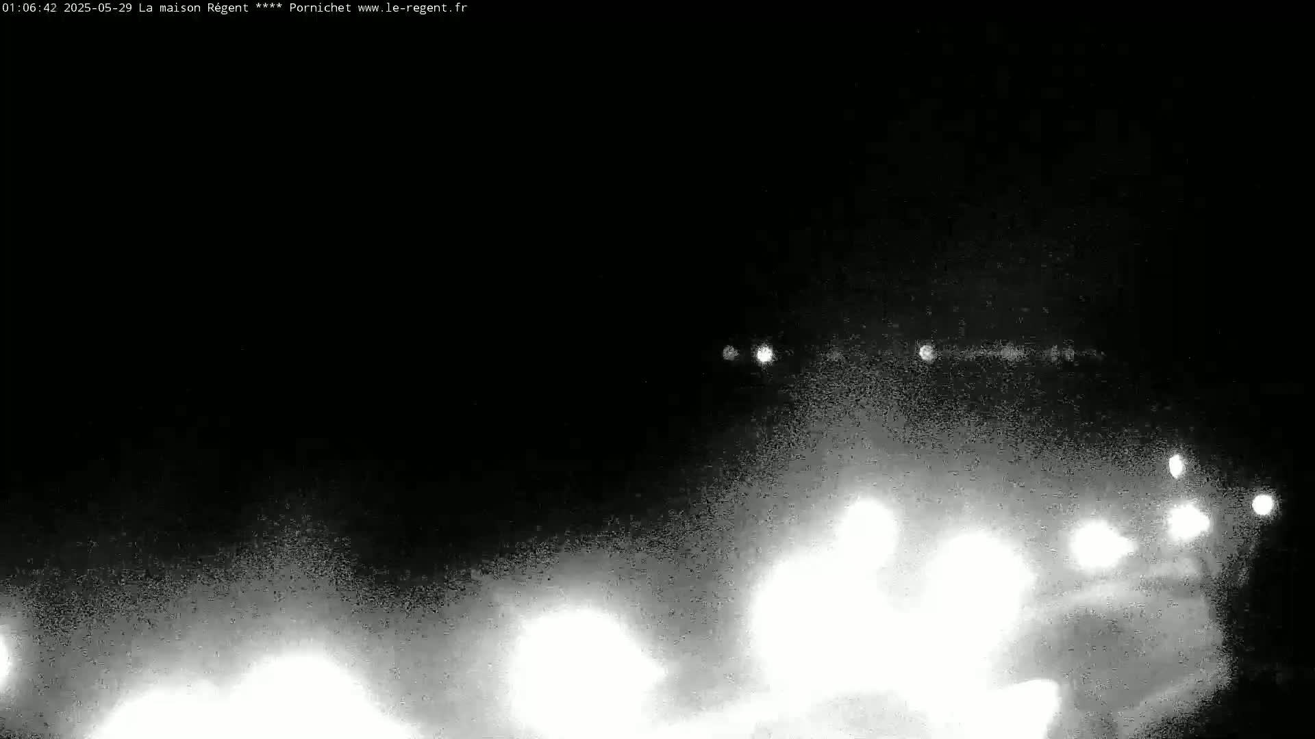 A nighttime, grainy image shows blurry white lights at the bottom of the frame that appear to be headlights of vehicles on a road, with a few fainter lights visible further away.