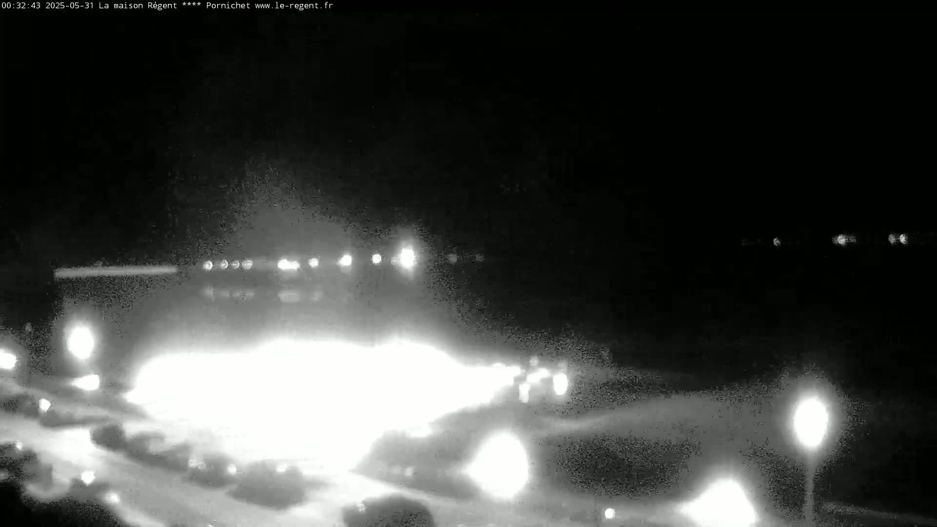 A nighttime, low-light view of a roadway with several vehicles, their headlights illuminating the scene.