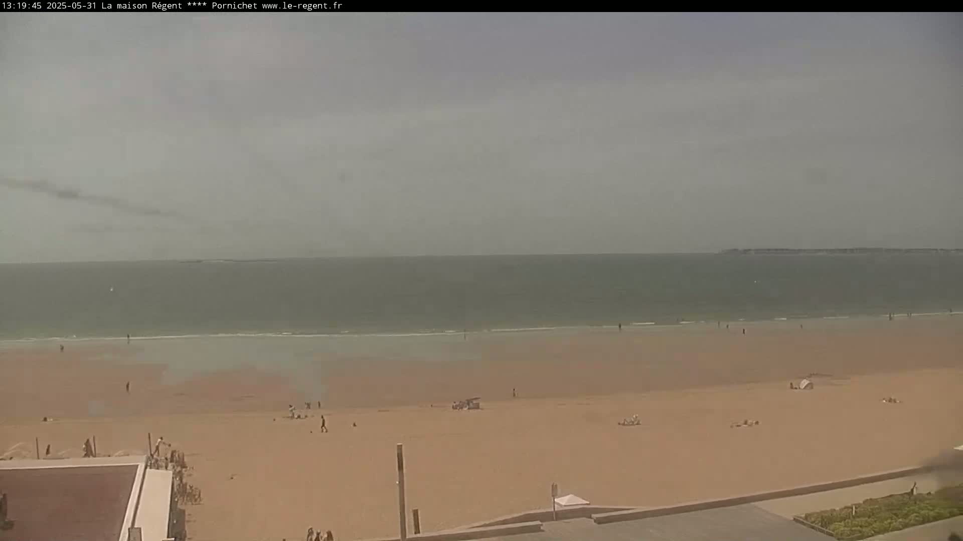 A wide sandy beach stretches to a calm, hazy ocean under an overcast sky.