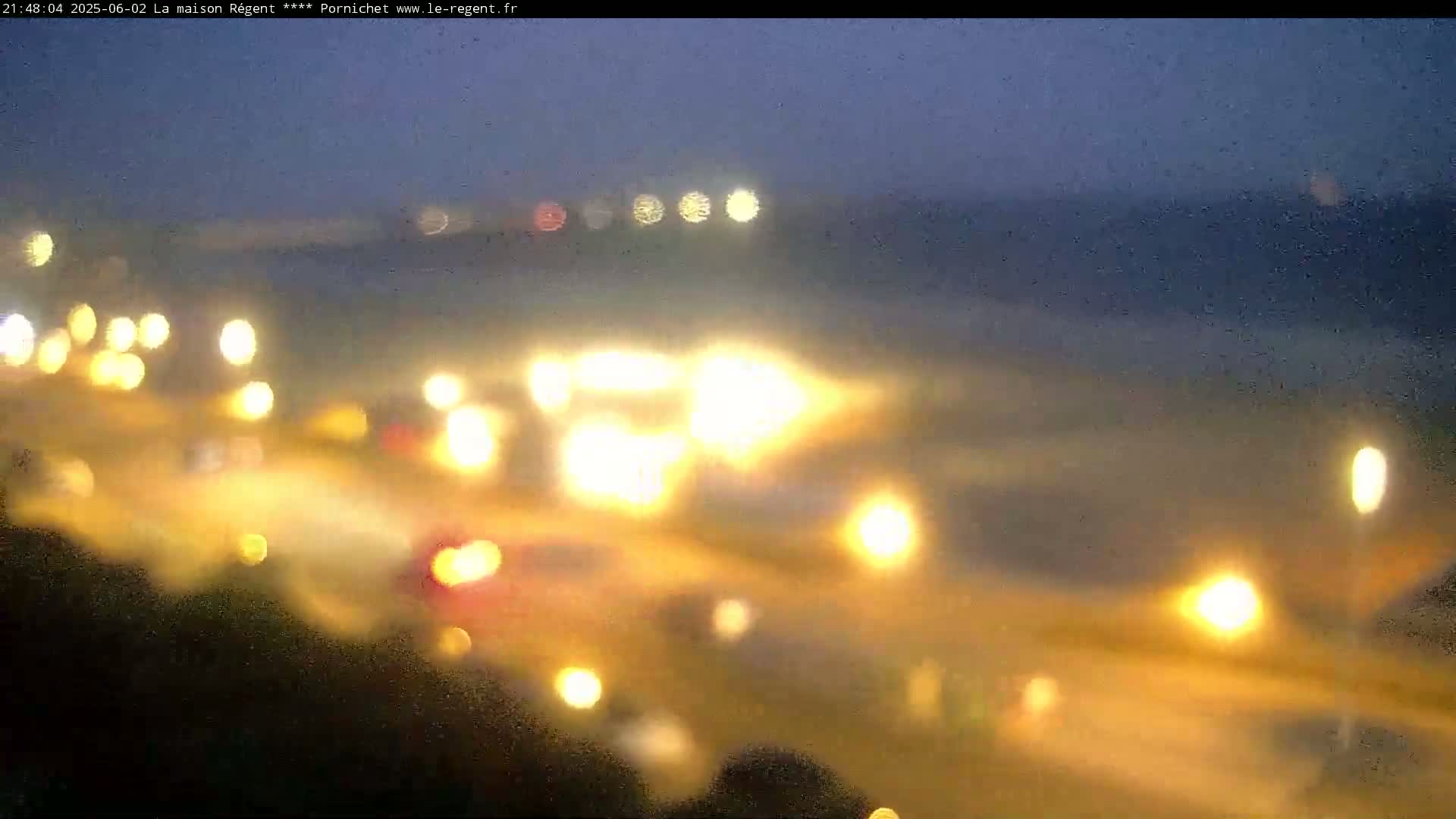 A blurry nighttime image shows out-of-focus lights from vehicles and streetlights, possibly on a road or in a town.