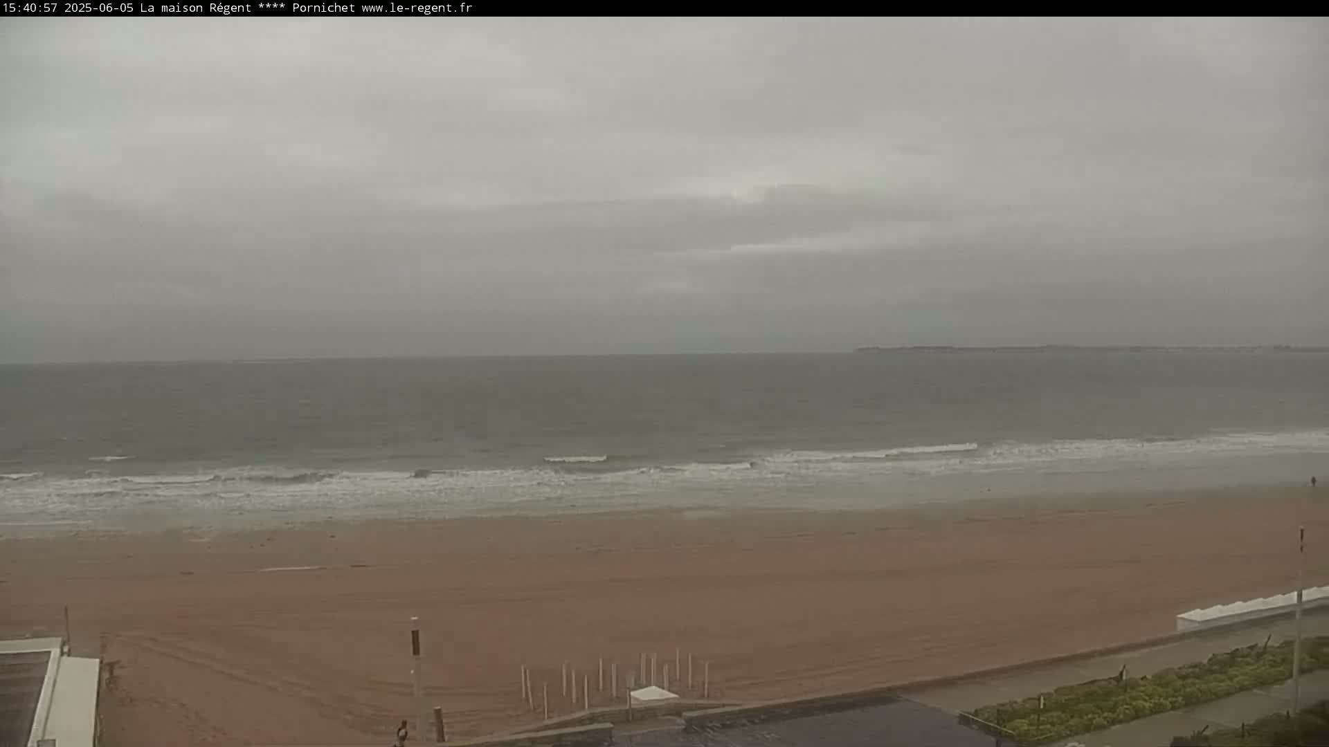 A wide shot of a sandy beach with gently lapping waves under an overcast sky.