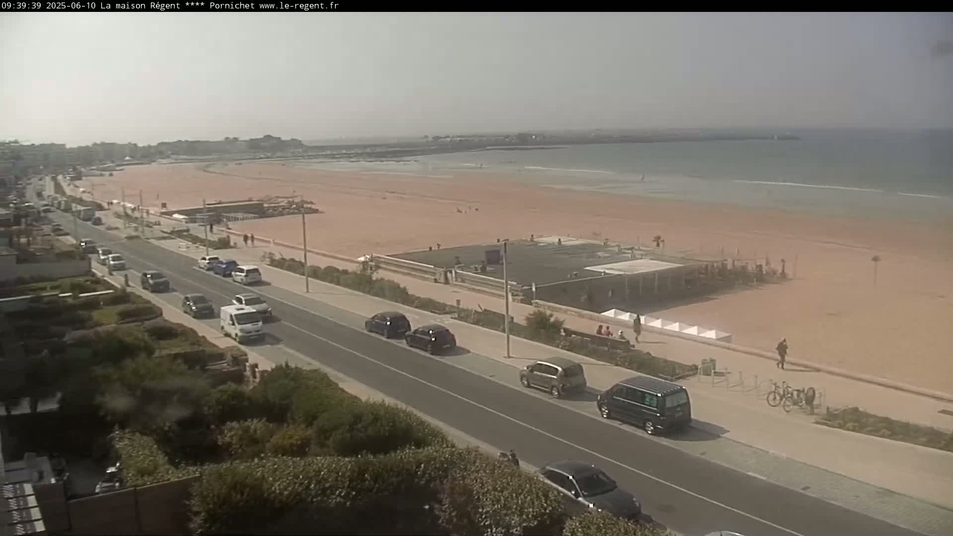 A sunny day overlooking a beach with cars parked along a road beside it.