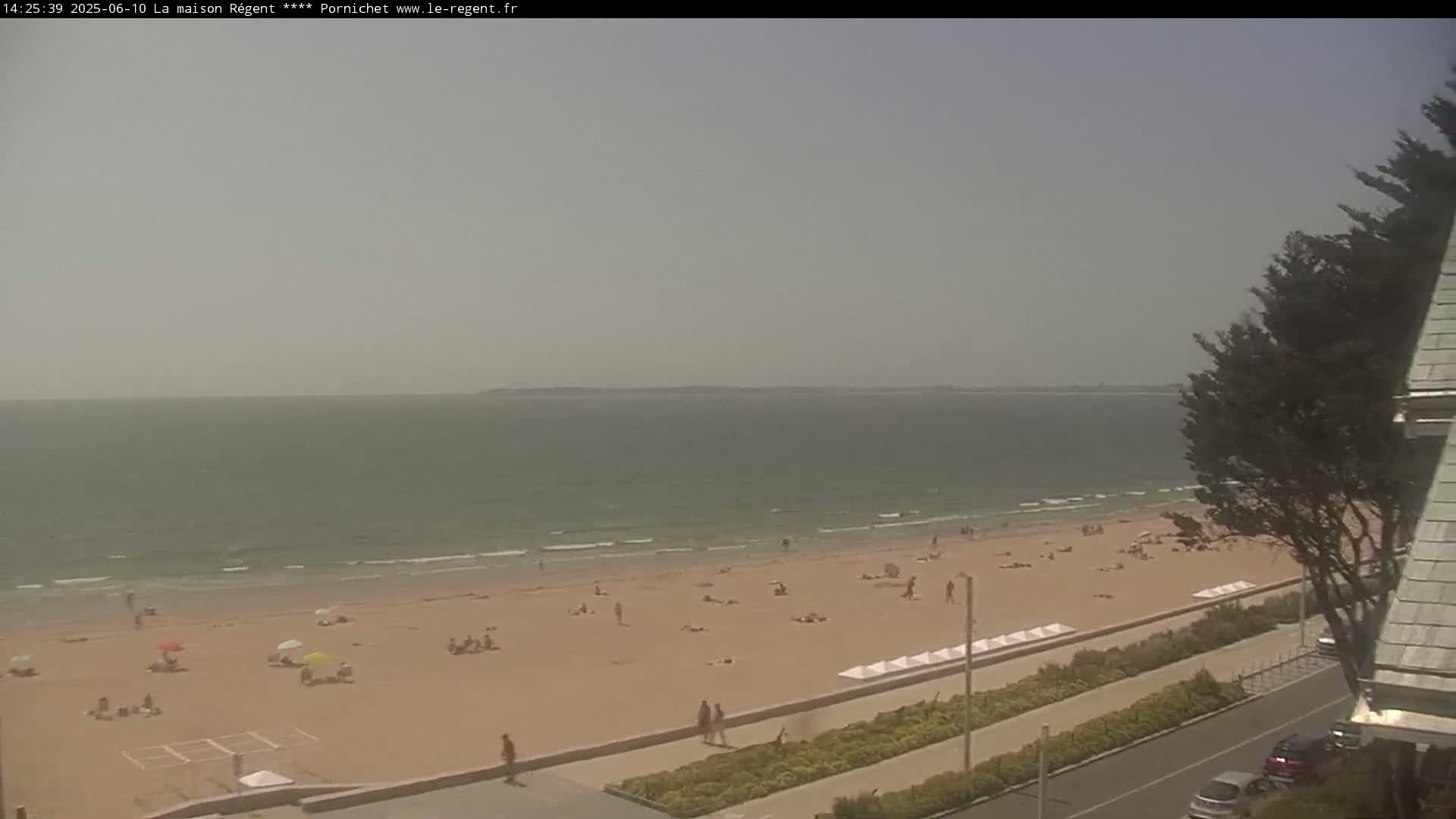 A hazy beach scene shows a sandy shore with scattered sunbathers, gentle waves lapping at the shoreline, and a calm sea extending to the horizon.
