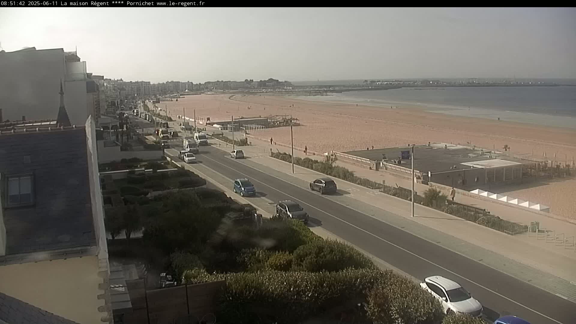 A sunny day at a beach with a road lined with cars running parallel to the shore.