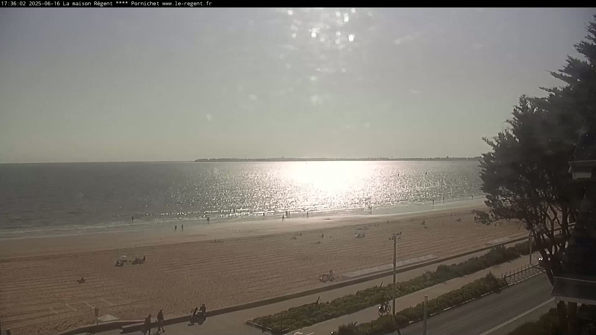 A sandy beach with scattered people is visible, extending to a calm sea under a bright, hazy sun.