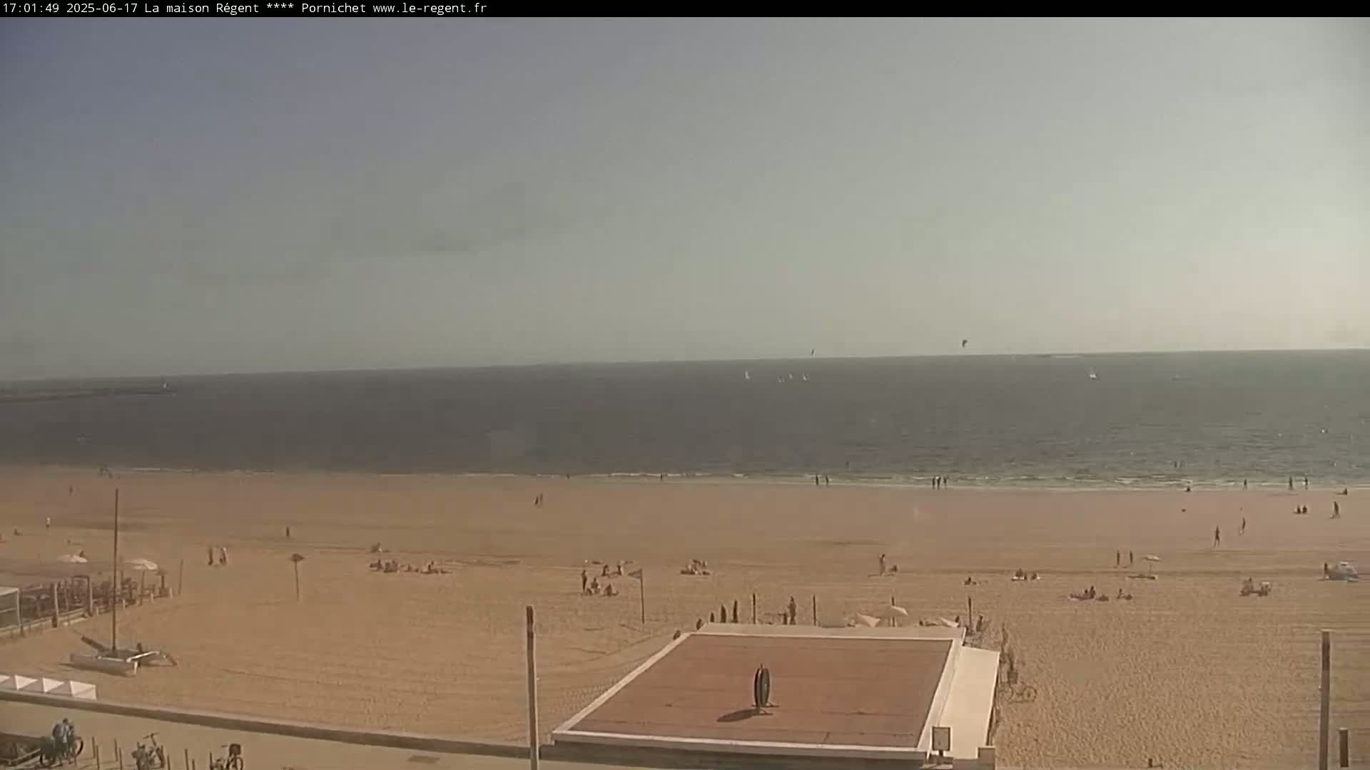 A sandy beach with scattered people is visible, extending to a calm, hazy ocean under a bright, clear sky.