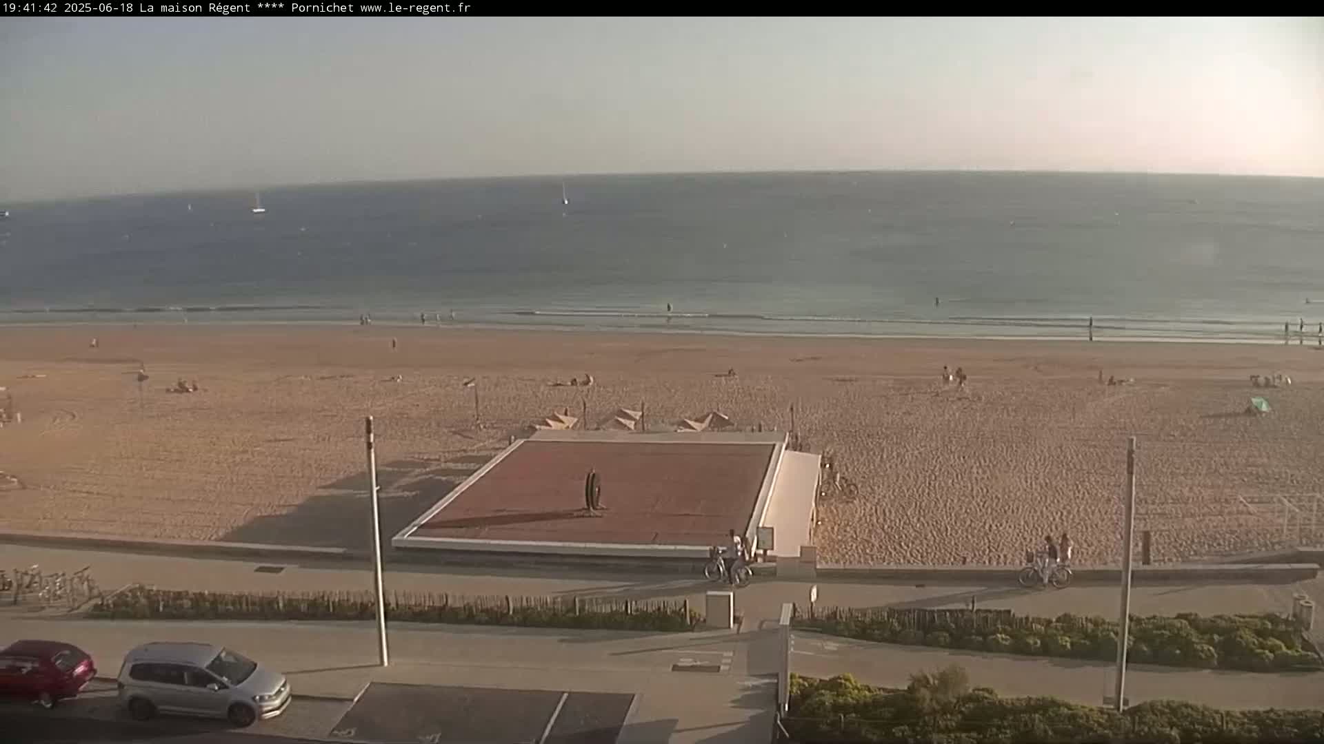A sandy beach with a few people on it is next to a calm ocean under a hazy sky.