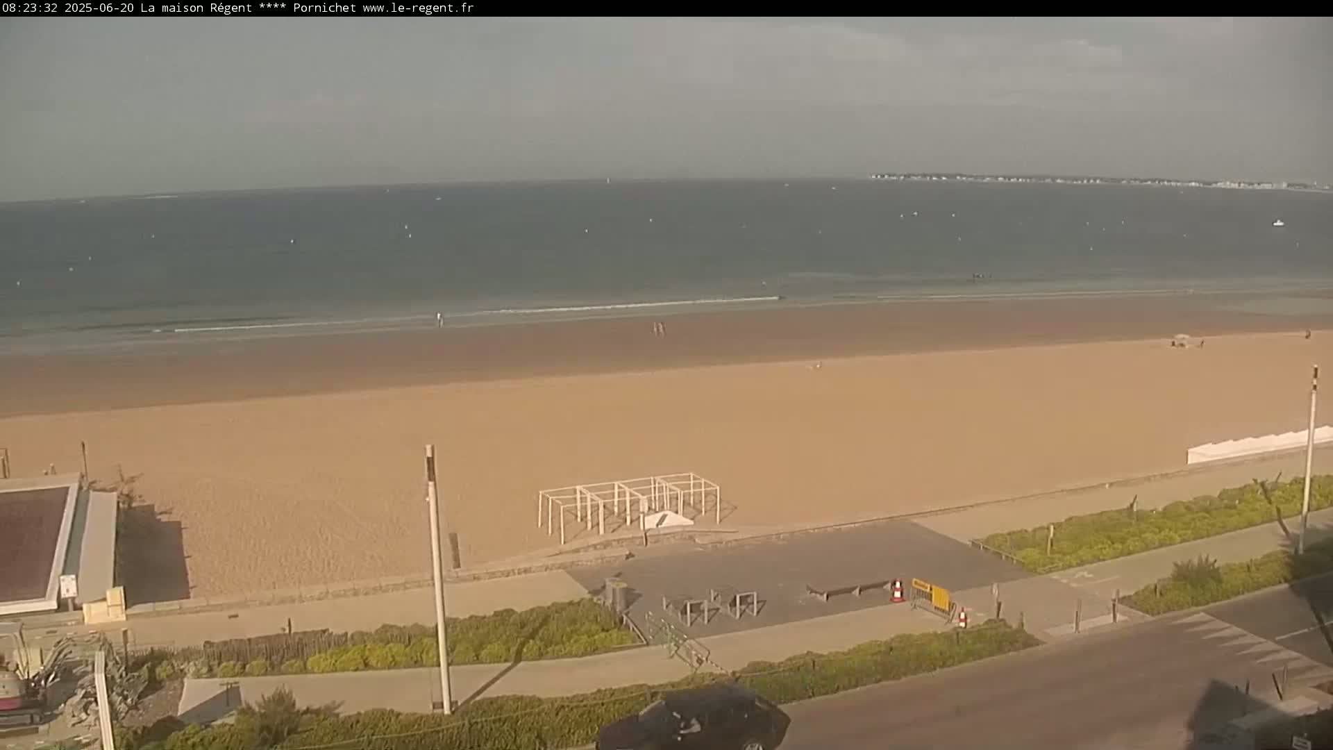 A mostly empty sandy beach stretches to a calm ocean under a hazy sky.
