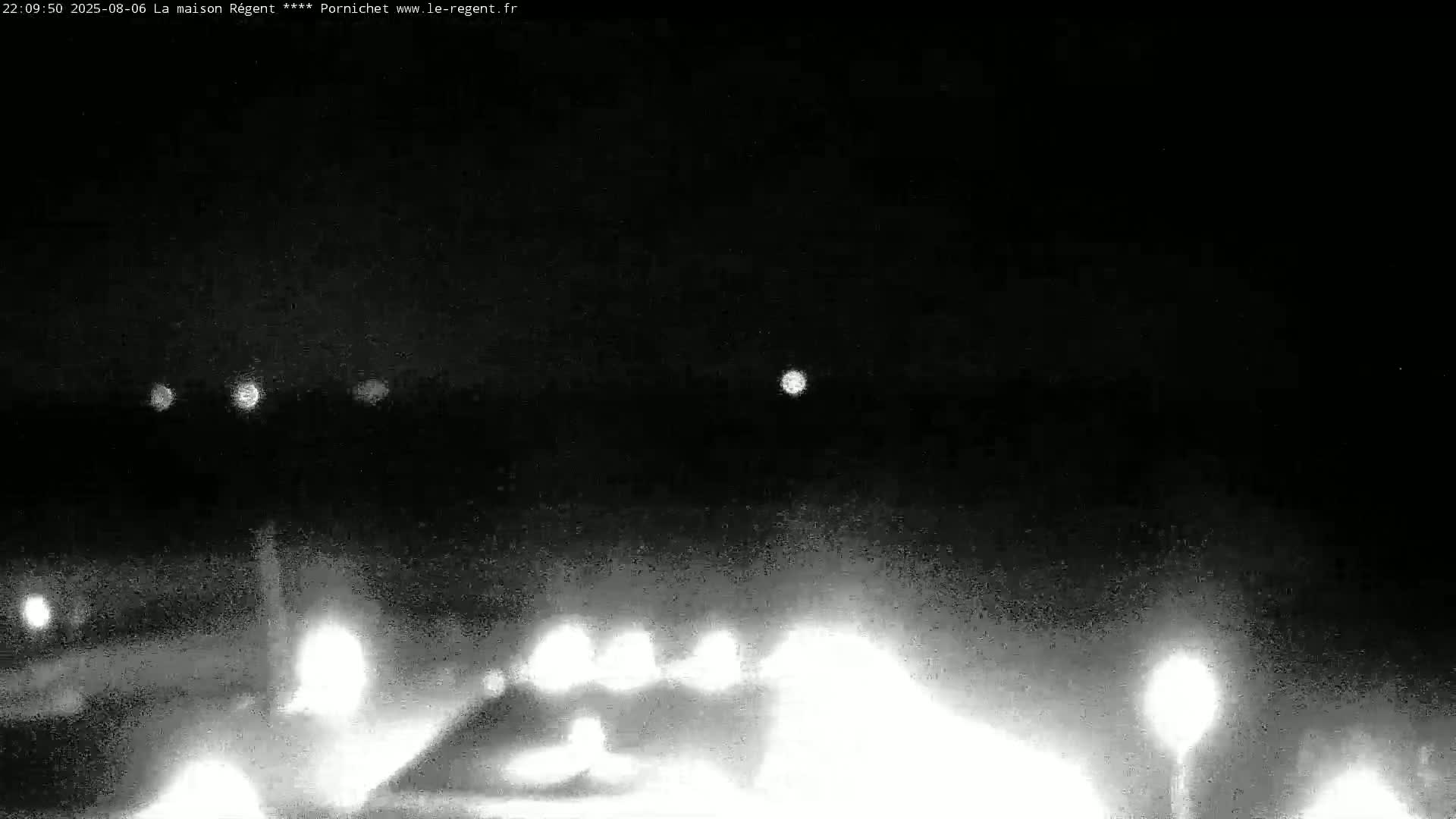 A nighttime, low-light view shows a road with headlights from approaching vehicles and streetlights visible in the distance under a dark sky.