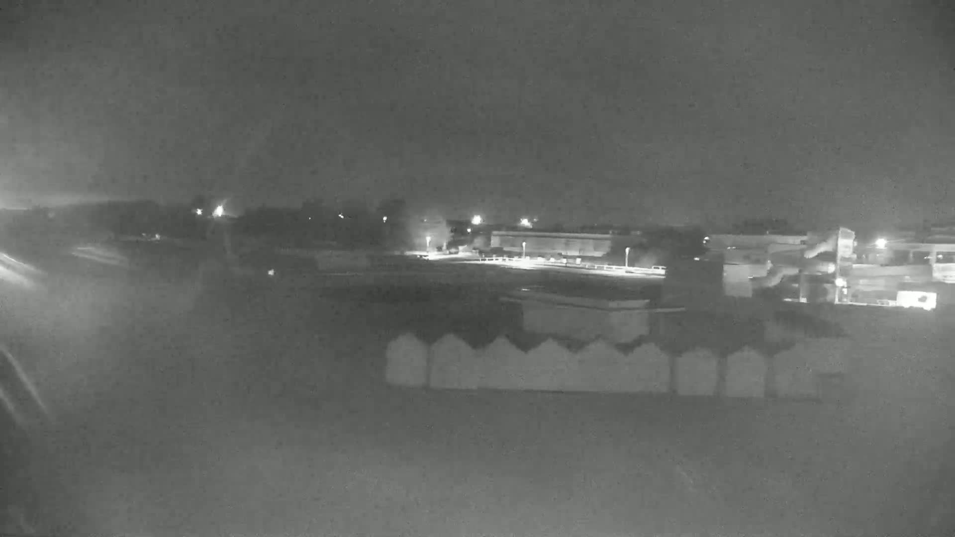 A nighttime, low-light view shows a paved area with a building and some trees, all under a dark sky.