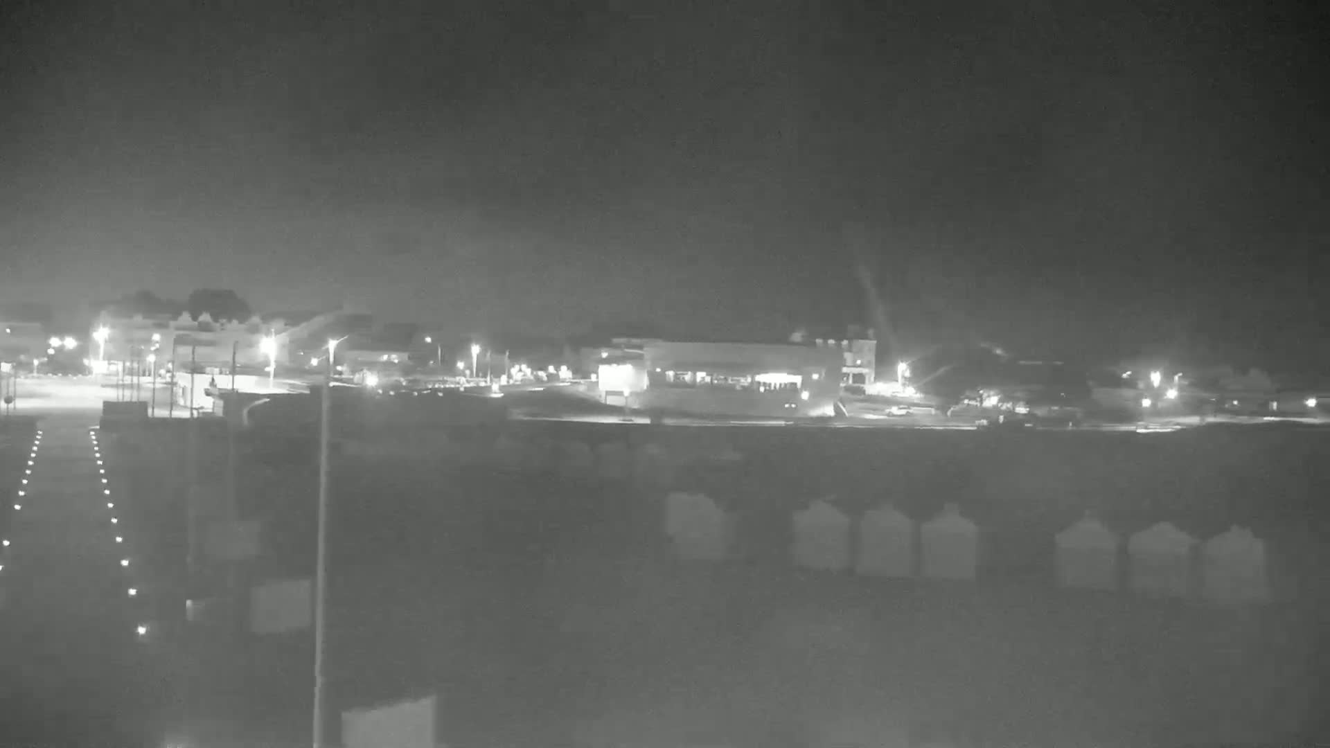 A nighttime, low-light view of a parking lot and buildings, with some vehicles present.