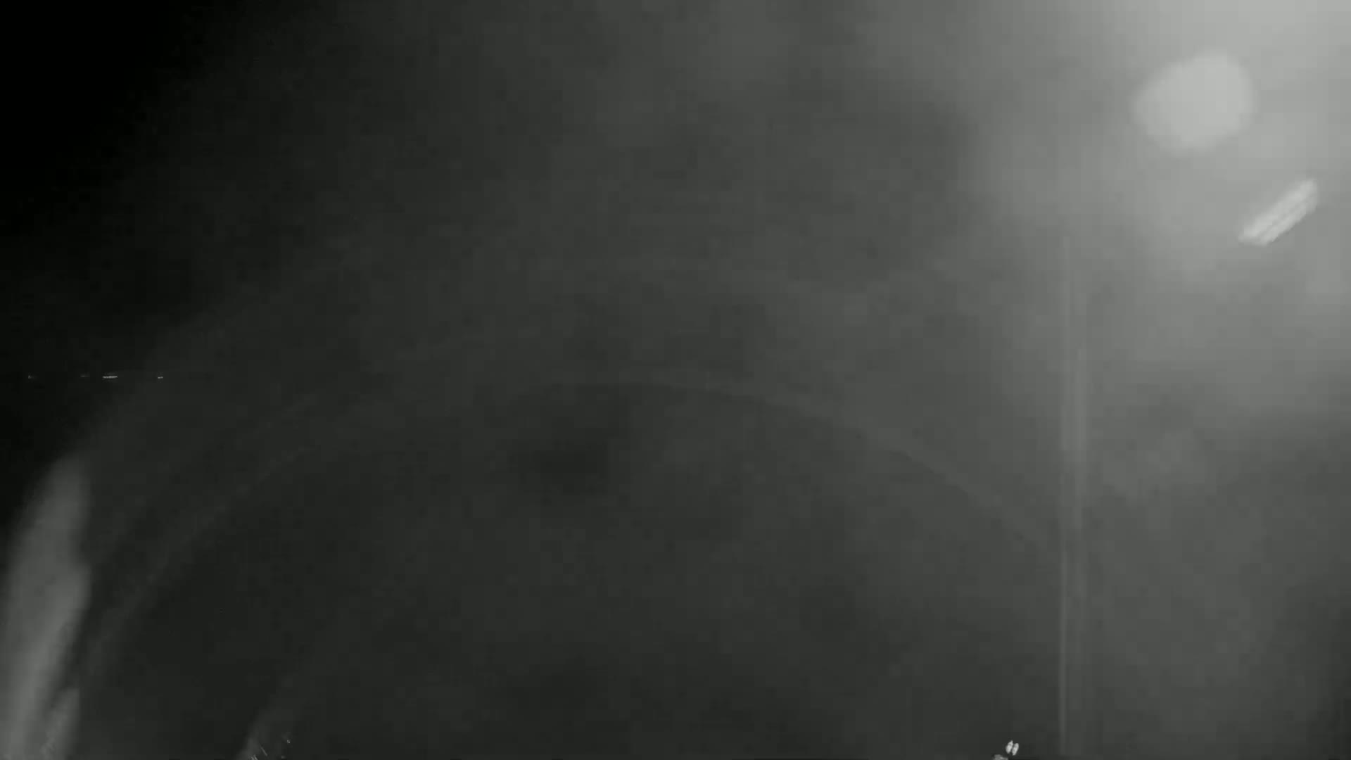 A hazy, dark grayscale image shows an indistinct, possibly industrial, scene illuminated by a bright light source.