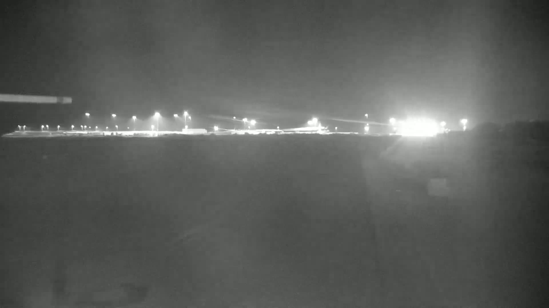 A nighttime, low-light view of a brightly lit, flat expanse of land with numerous light posts.