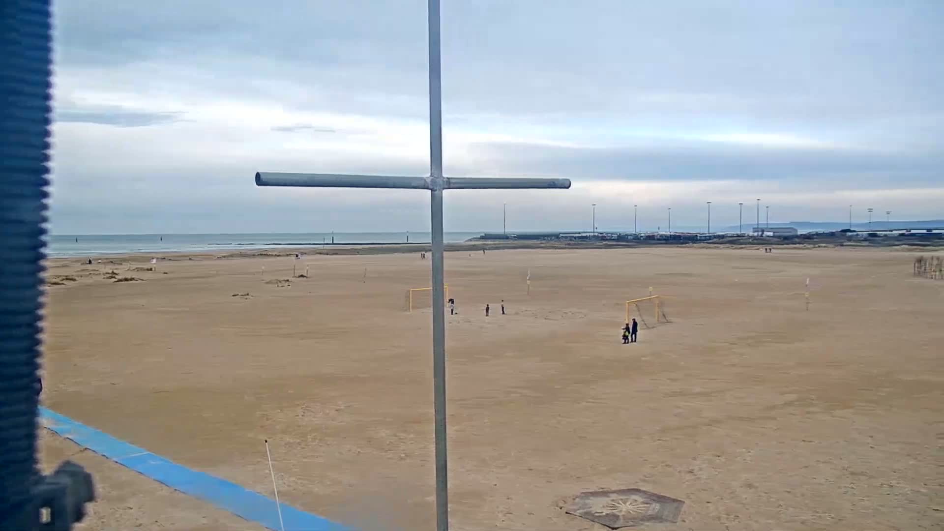 A sandy beach with a few people playing soccer under a cloudy sky.