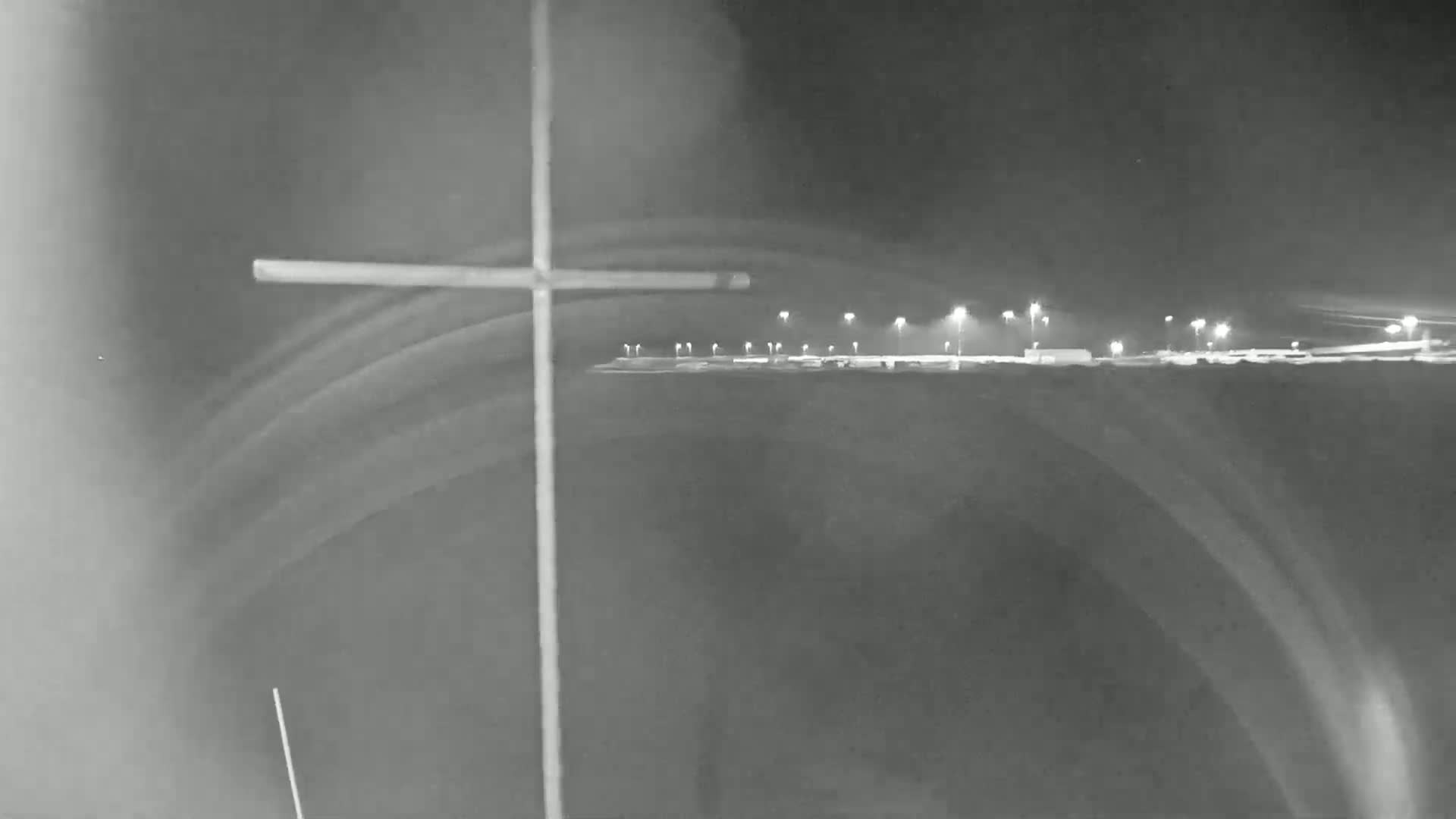 A nighttime, low-light image shows a cross-shaped object in the foreground with a distant, illuminated area in the background.