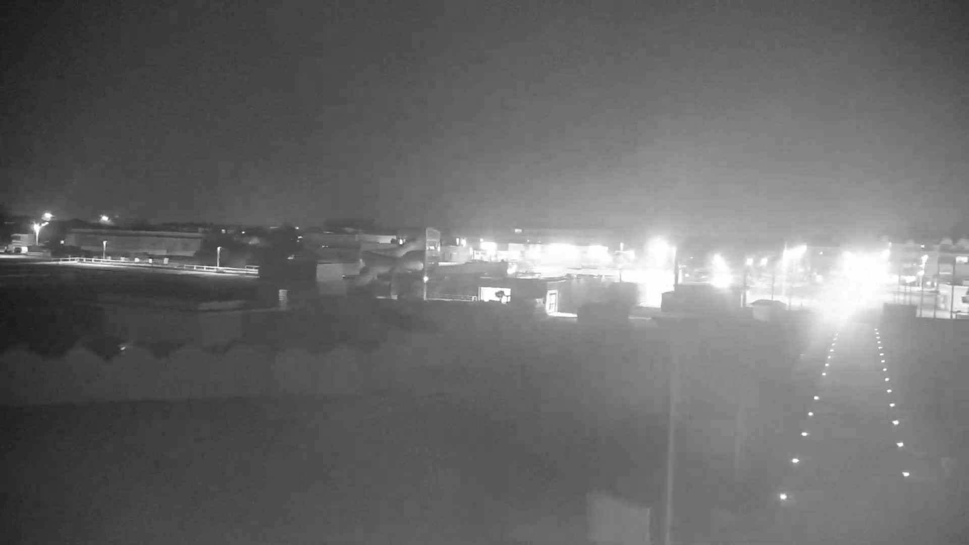 A nighttime, hazy view of a road with illuminated lane markings leading to a distant, dimly lit industrial area.