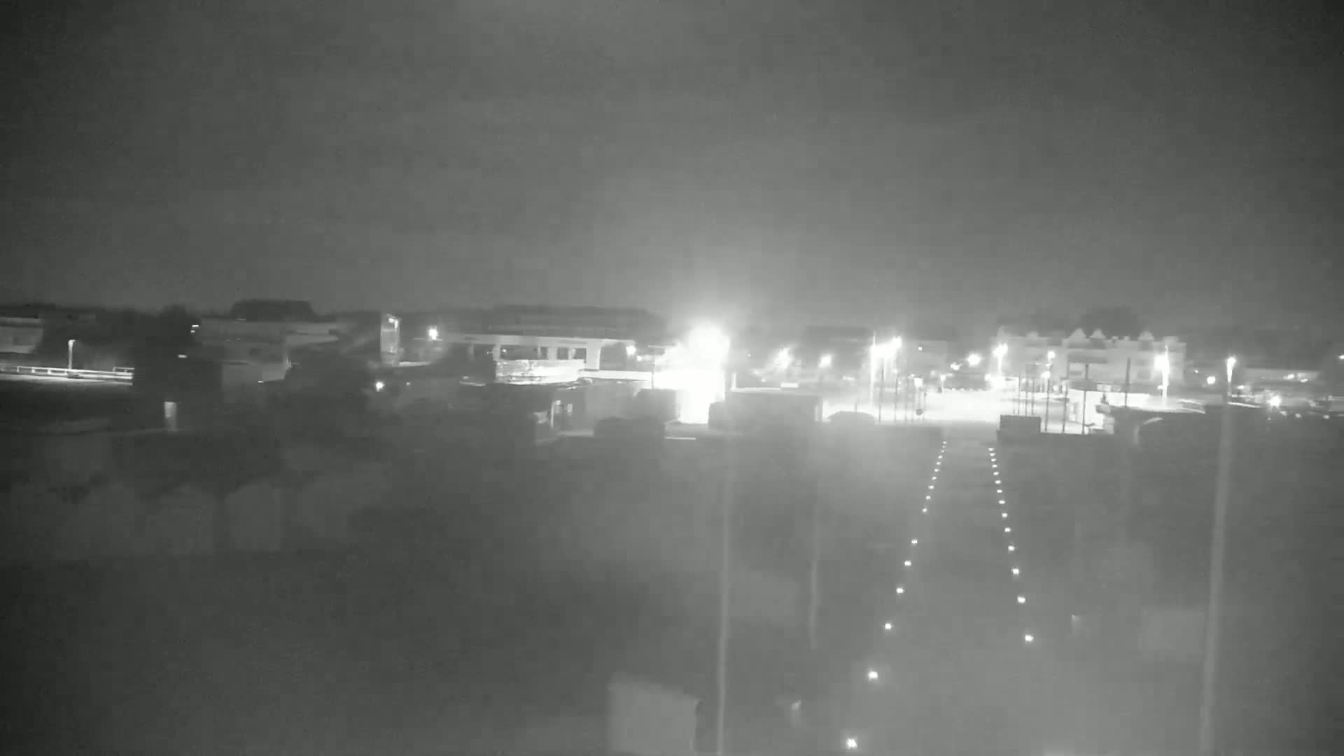 A nighttime, low-light view of a mostly empty parking lot and surrounding buildings.