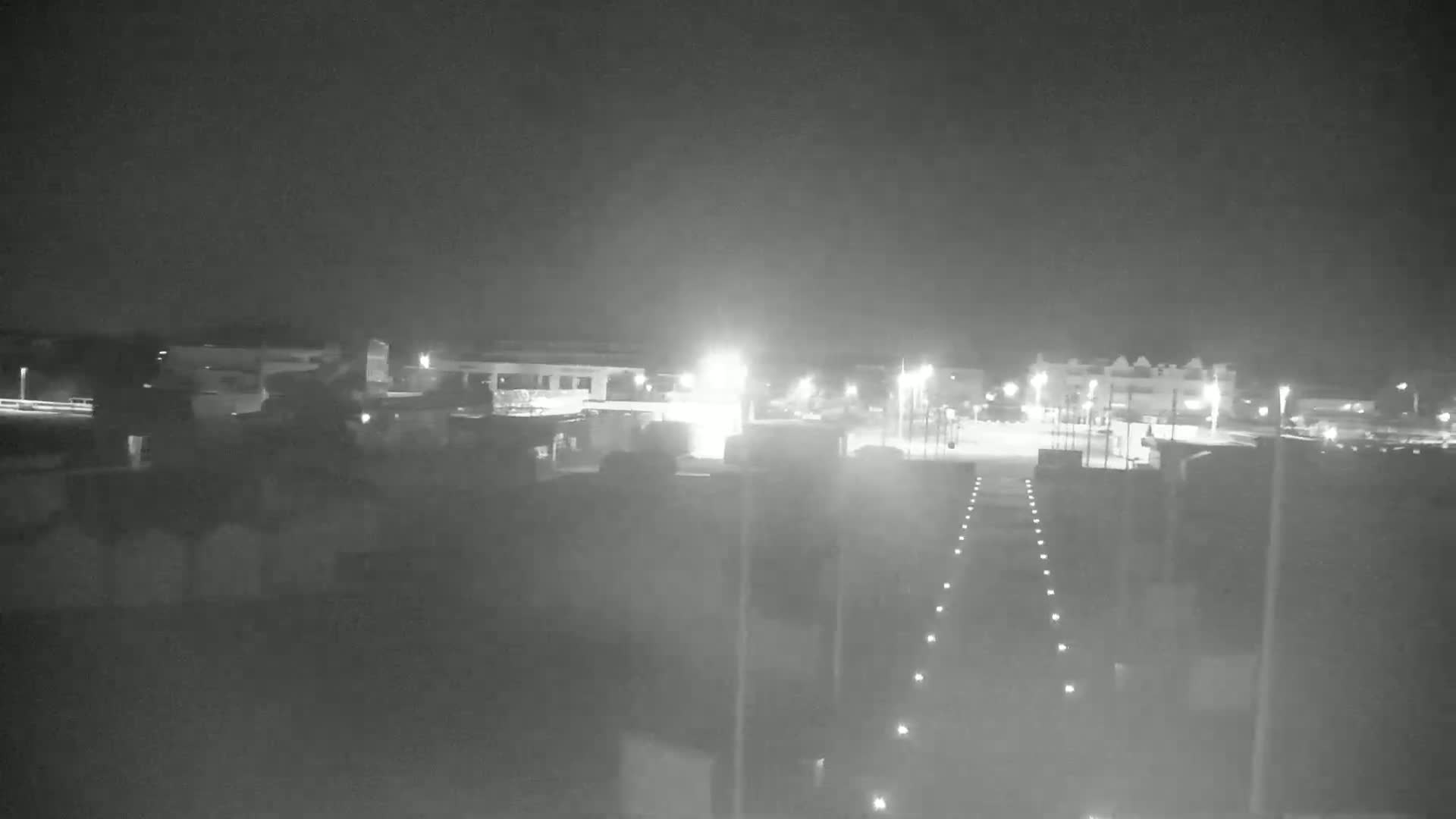 A nighttime, low-light view of a mostly empty parking lot and surrounding buildings.