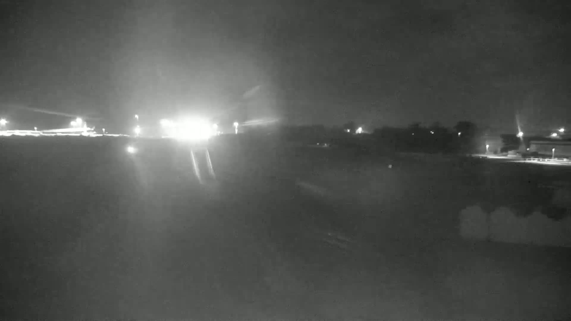 A nighttime, dimly lit highway scene with some trees and buildings in the background.