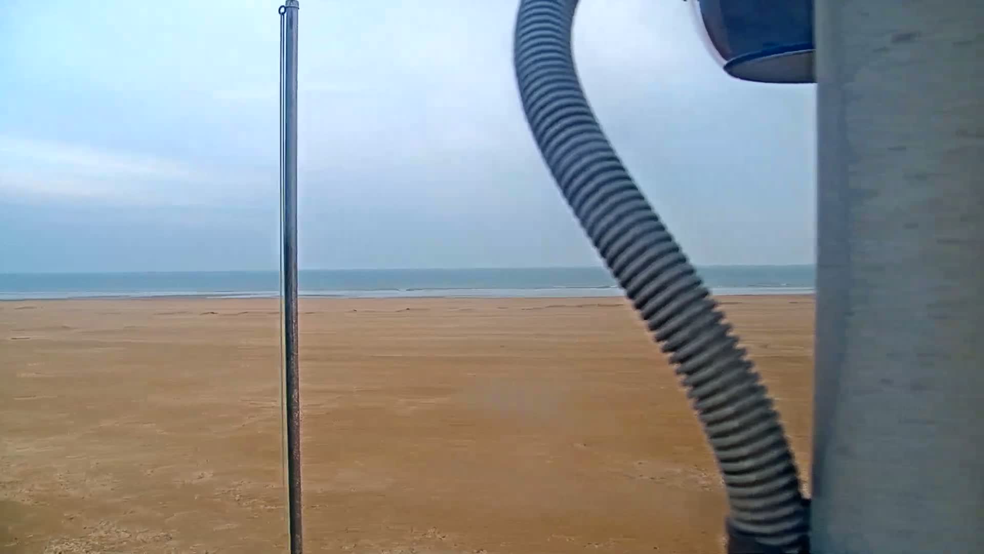 A long, sandy beach stretches to a calm, light-blue ocean under a mostly clear sky.
