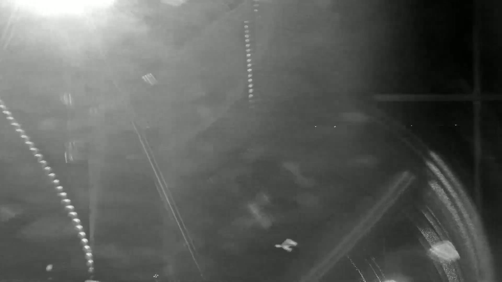 A blurry, nighttime image shows streaks of light and what appears to be snow or rain falling in front of a dark, indistinct background.