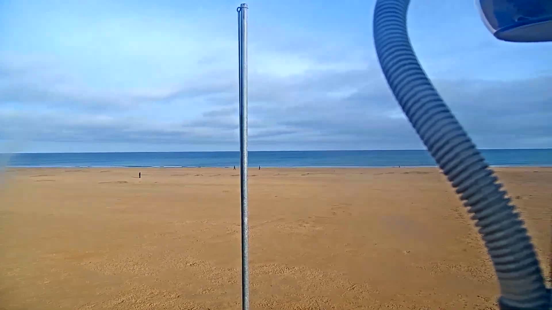 A mostly clear sky overlooks a wide expanse of sandy beach and calm ocean.