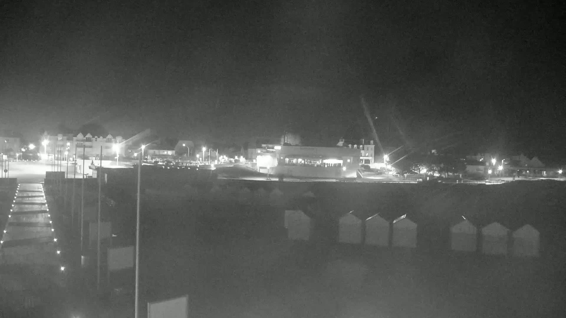 A nighttime, low-light view of a beach area with several buildings, a parking lot, and beach huts.