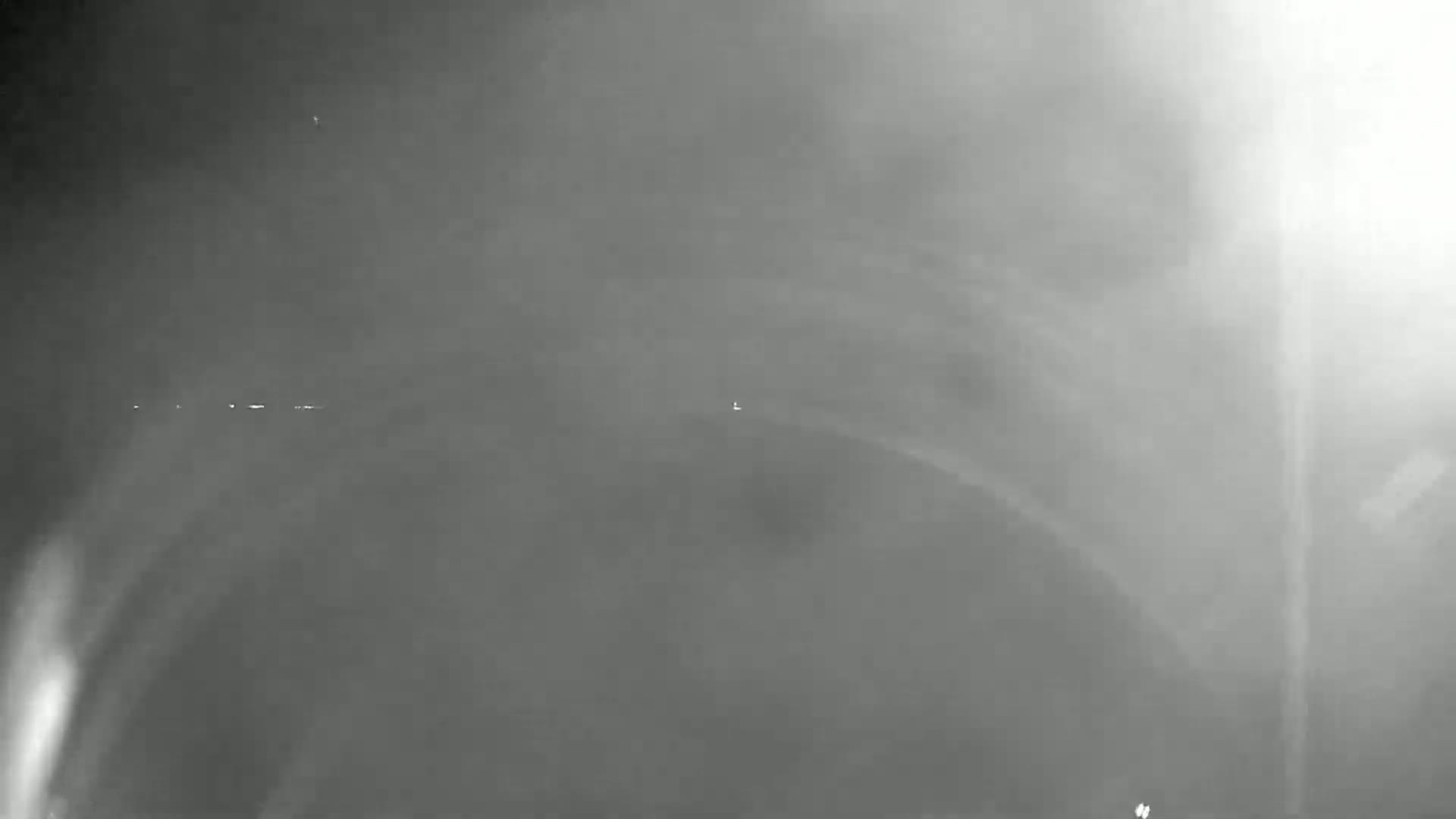 A hazy, dark gray image shows a dimly lit landscape with faint lights on the horizon.