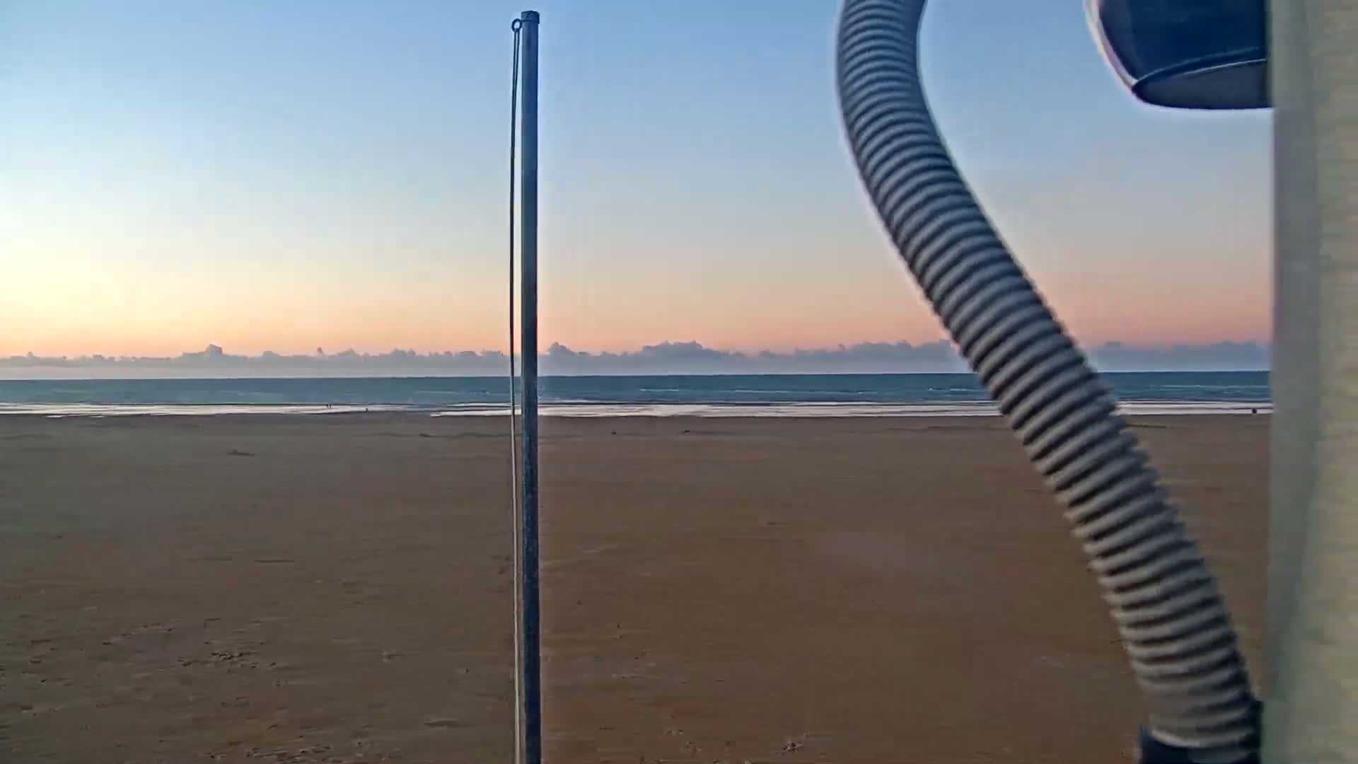 A calm ocean meets a wide, sandy beach under a clear, sunset sky.