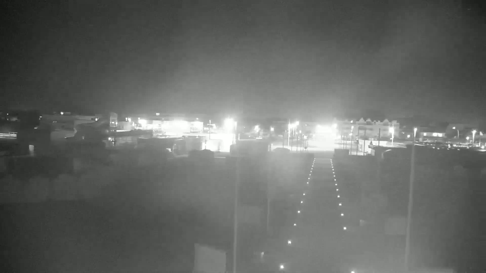 A nighttime, hazy view of a dimly lit parking lot and buildings.