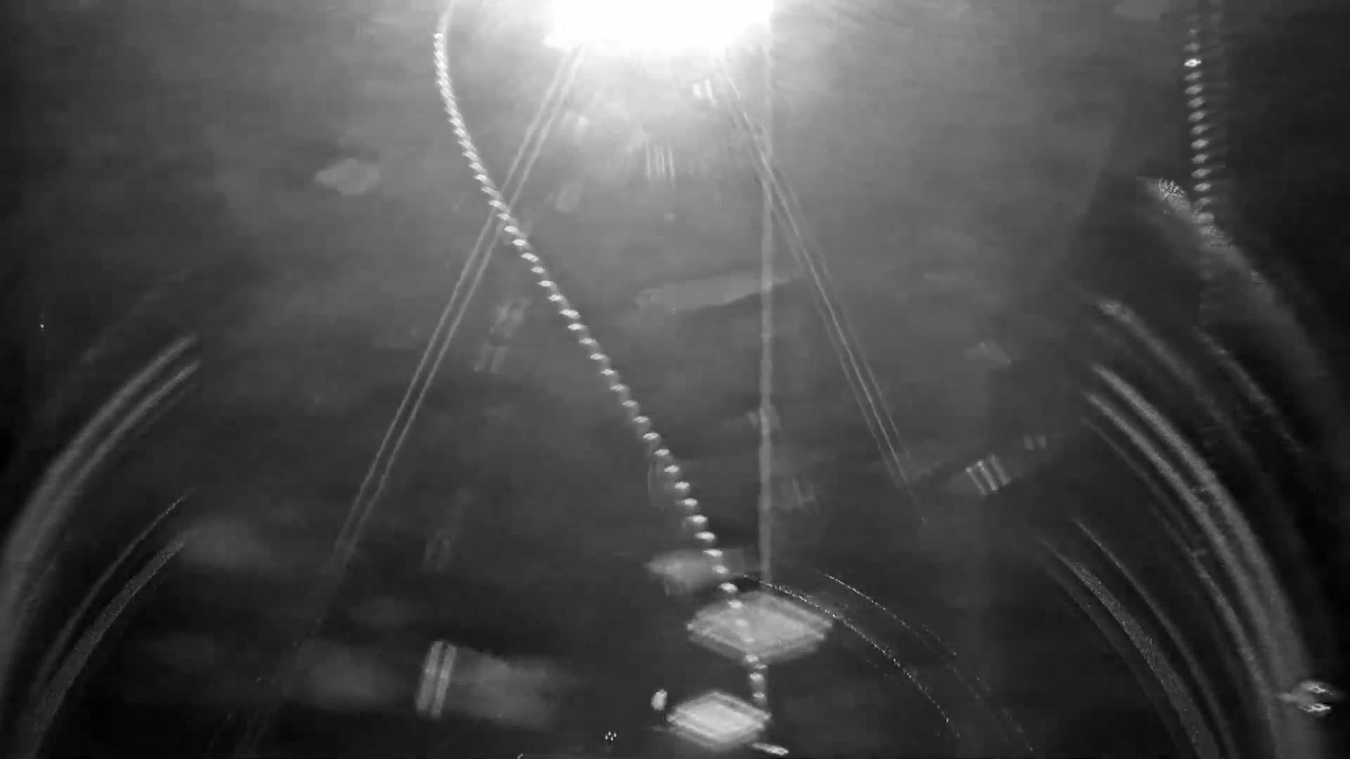 A blurry, nighttime image shows a series of lights streaking across a dark surface, possibly a road or tunnel.