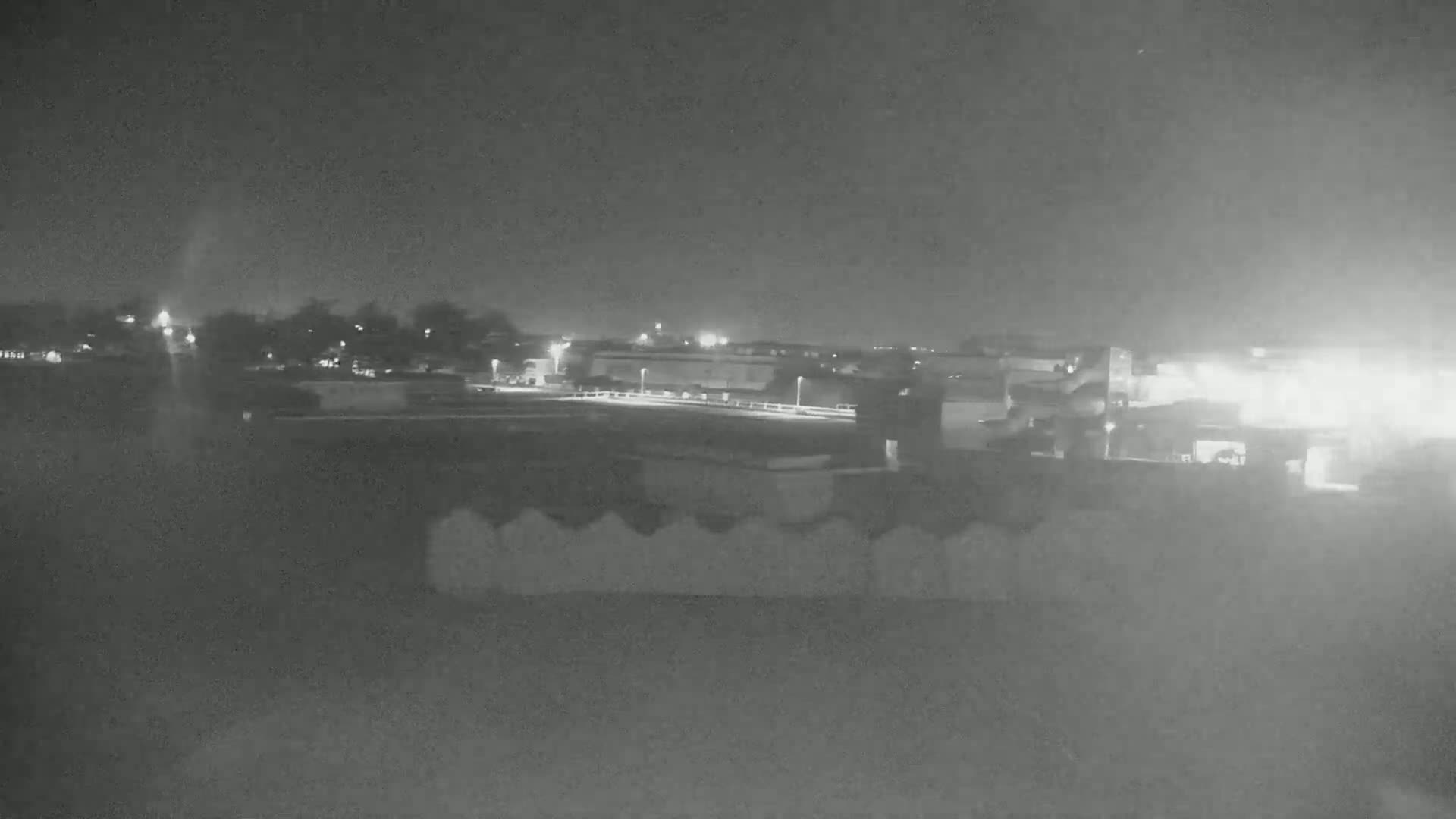 At night, a train is visible in the distance, beyond a low wall, under a dark, overcast sky.