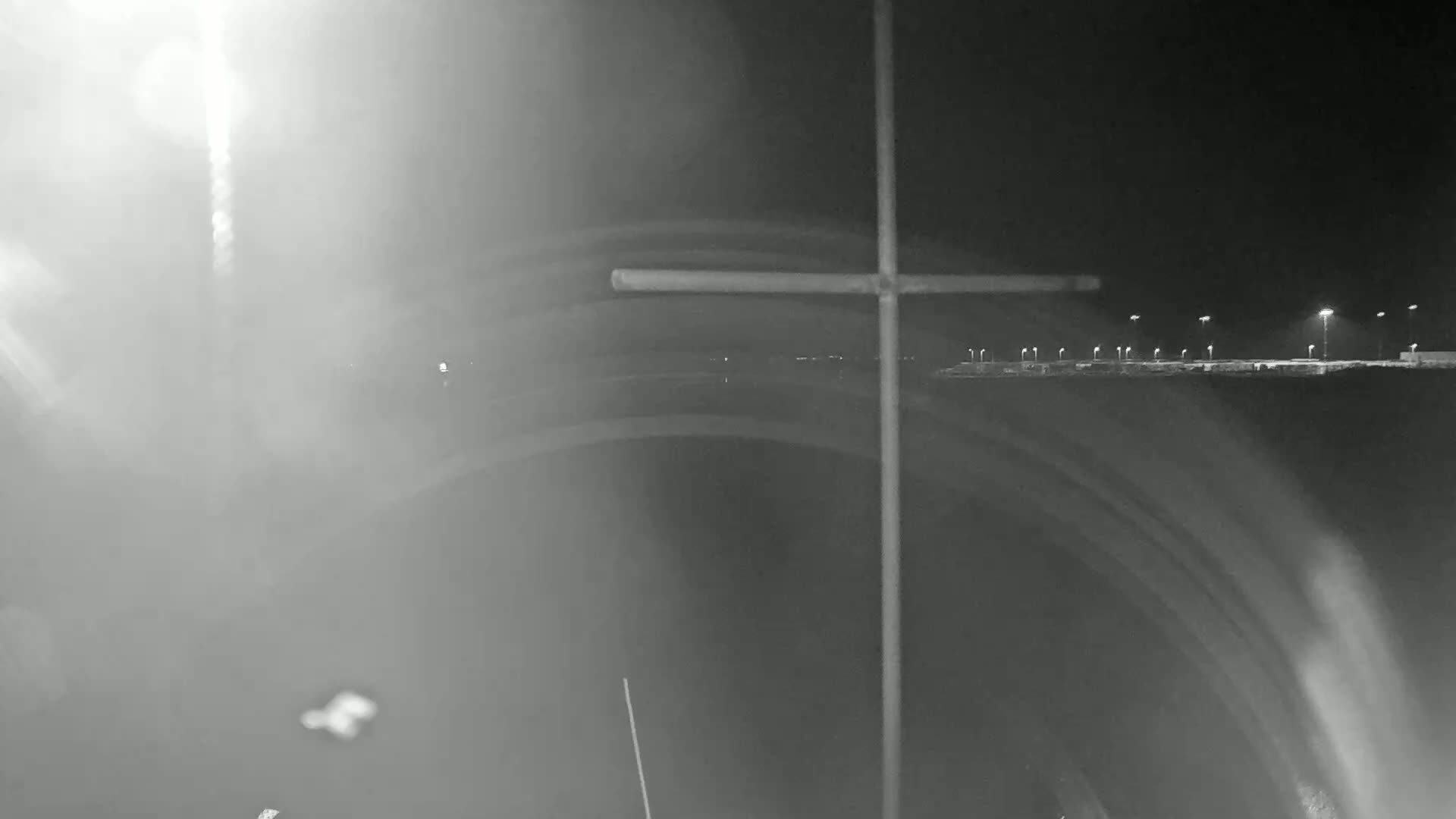 A blurry nighttime image shows a cross-shaped structure in the foreground with a distant, dimly lit parking lot visible through a hazy atmosphere.