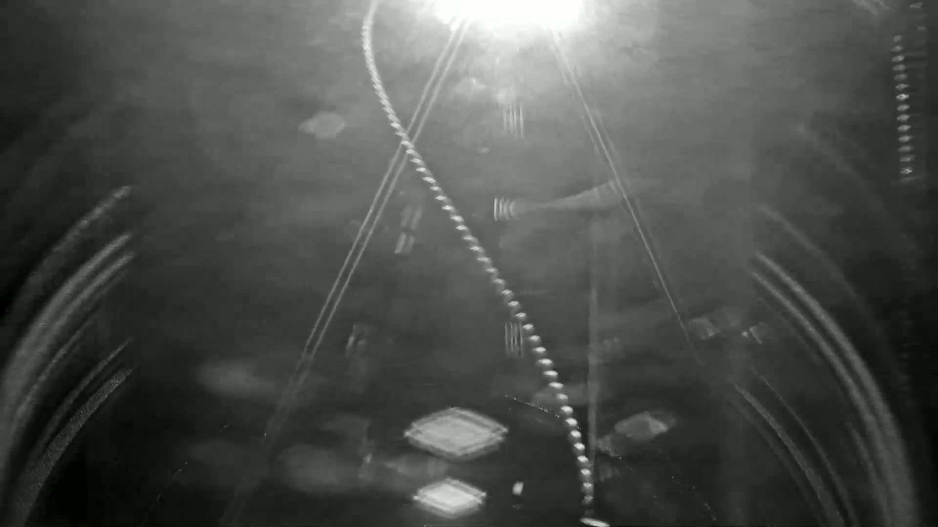 A blurry, nighttime image shows a long, beaded chain-like object curving through a dark, possibly enclosed space with bright light at the top.