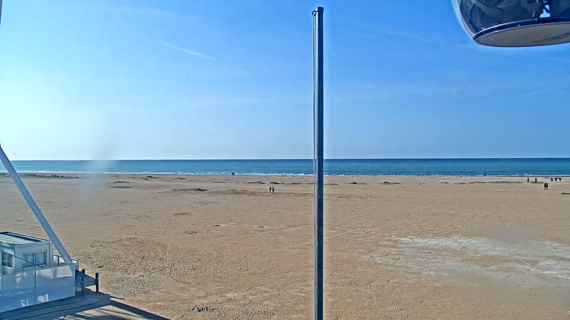 A wide sandy beach stretches to a calm, blue ocean under a clear blue sky.