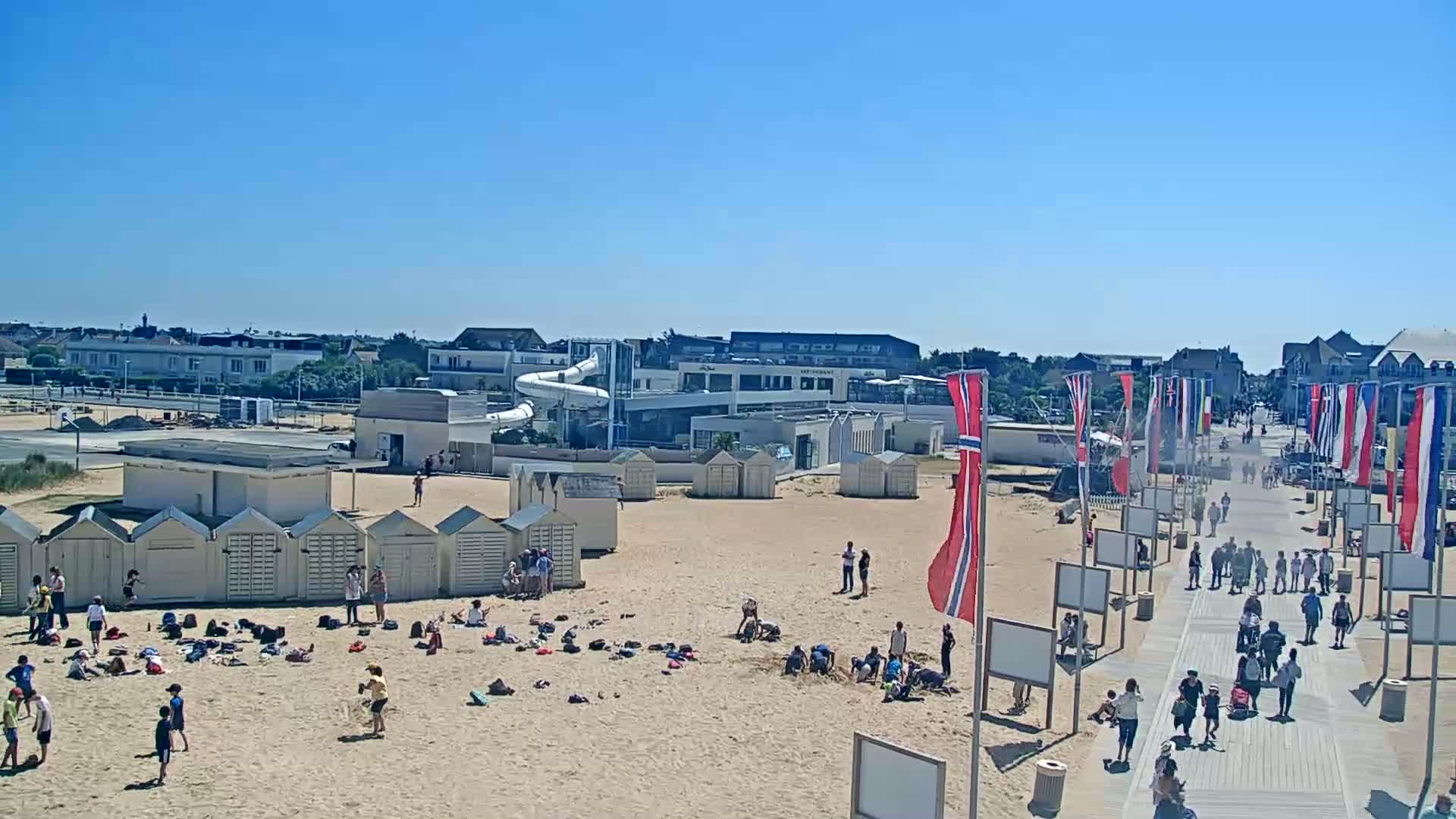 A sandy beach with people, beach huts, and a water park is visible on a sunny day.