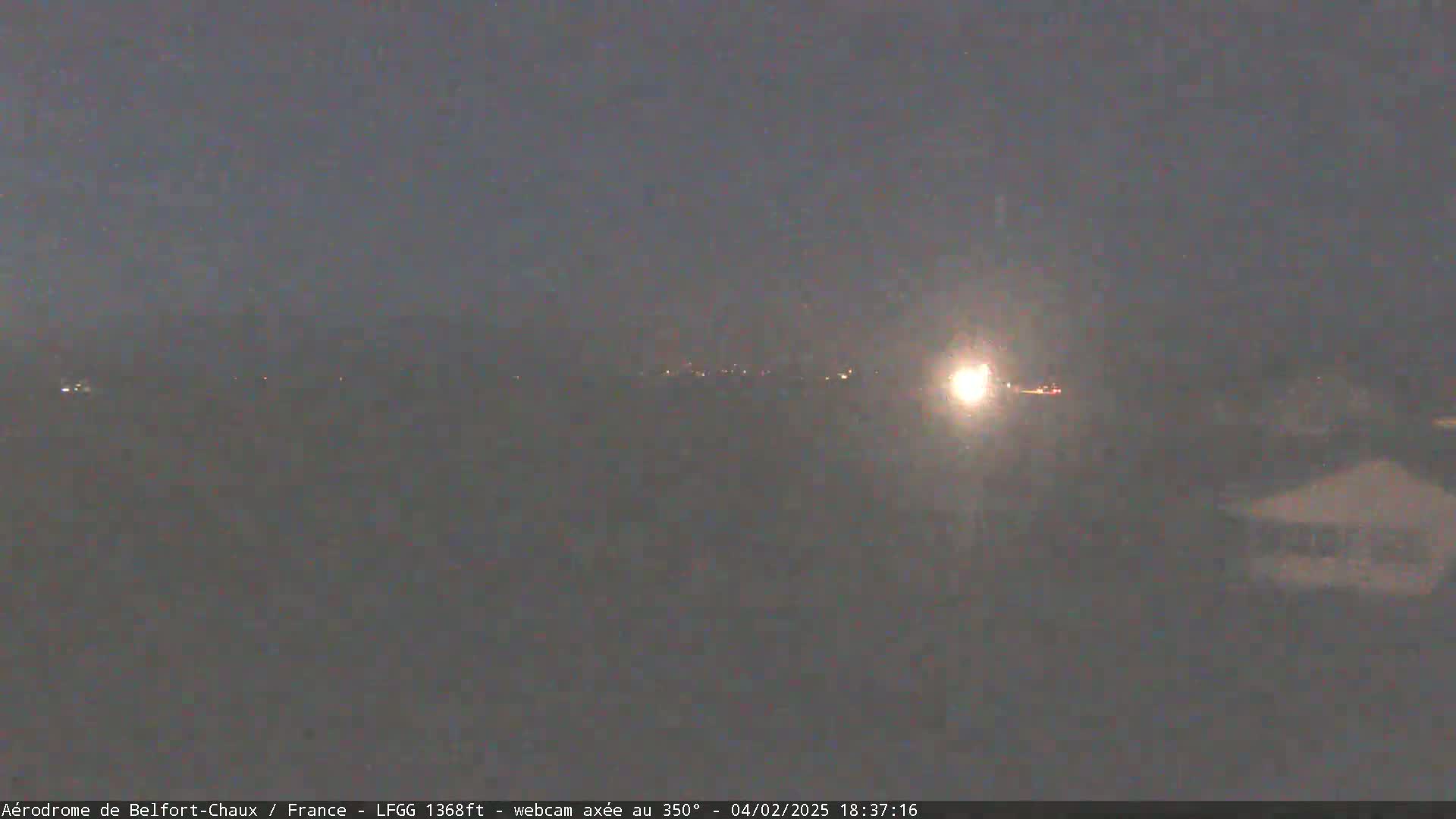 A nighttime, hazy view shows distant lights in the middle distance, with a brighter light source to the right.