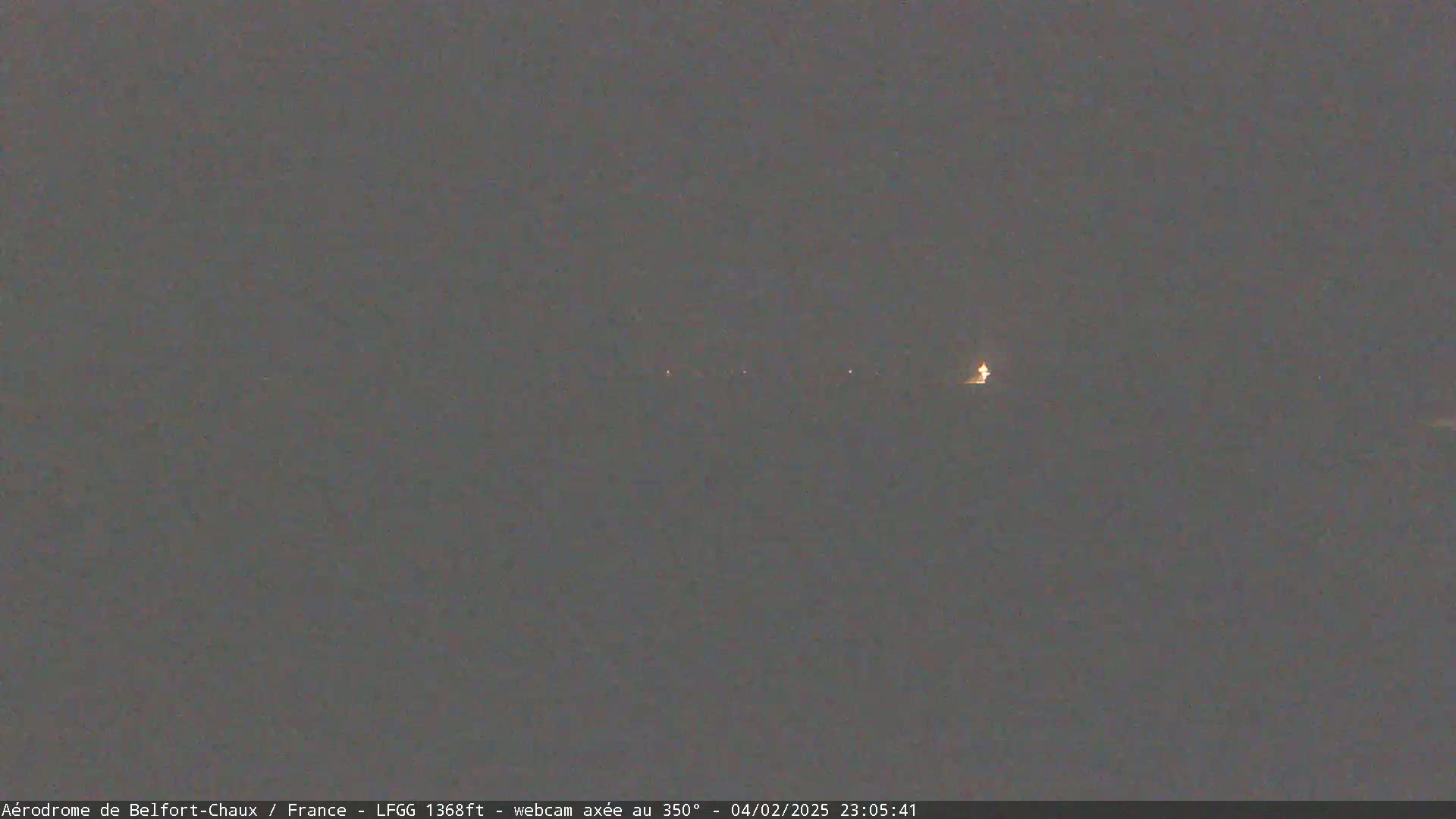 A nighttime, dimly lit landscape is visible under a dark, overcast sky, with a few faint lights in the distance.