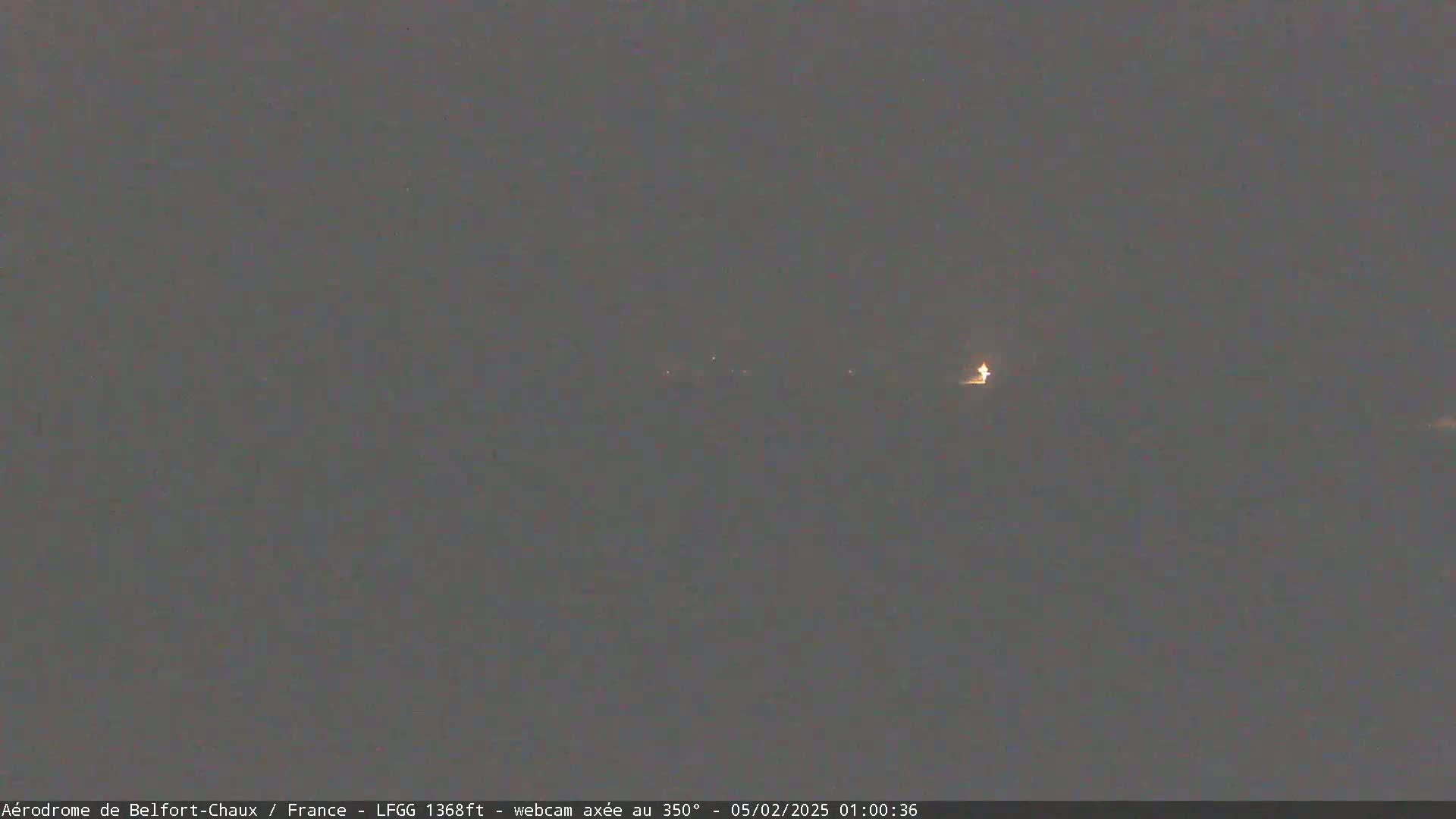 A dark, nighttime scene shows a few faint lights in the distance under a gray sky.