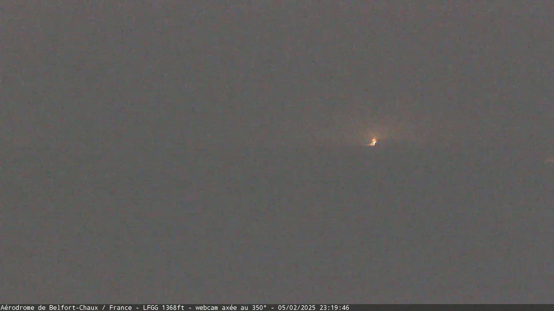A dimly lit, nighttime scene shows a small, distant light source on a hazy horizon.
