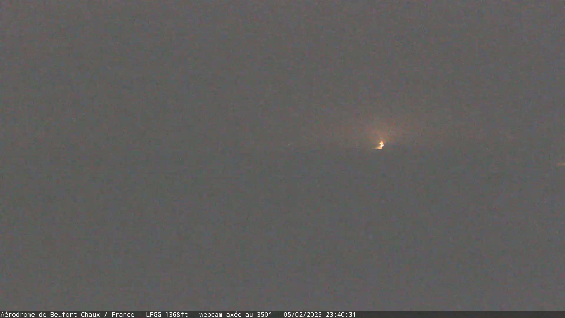 A dim light is visible in the distance on a dark, overcast night.