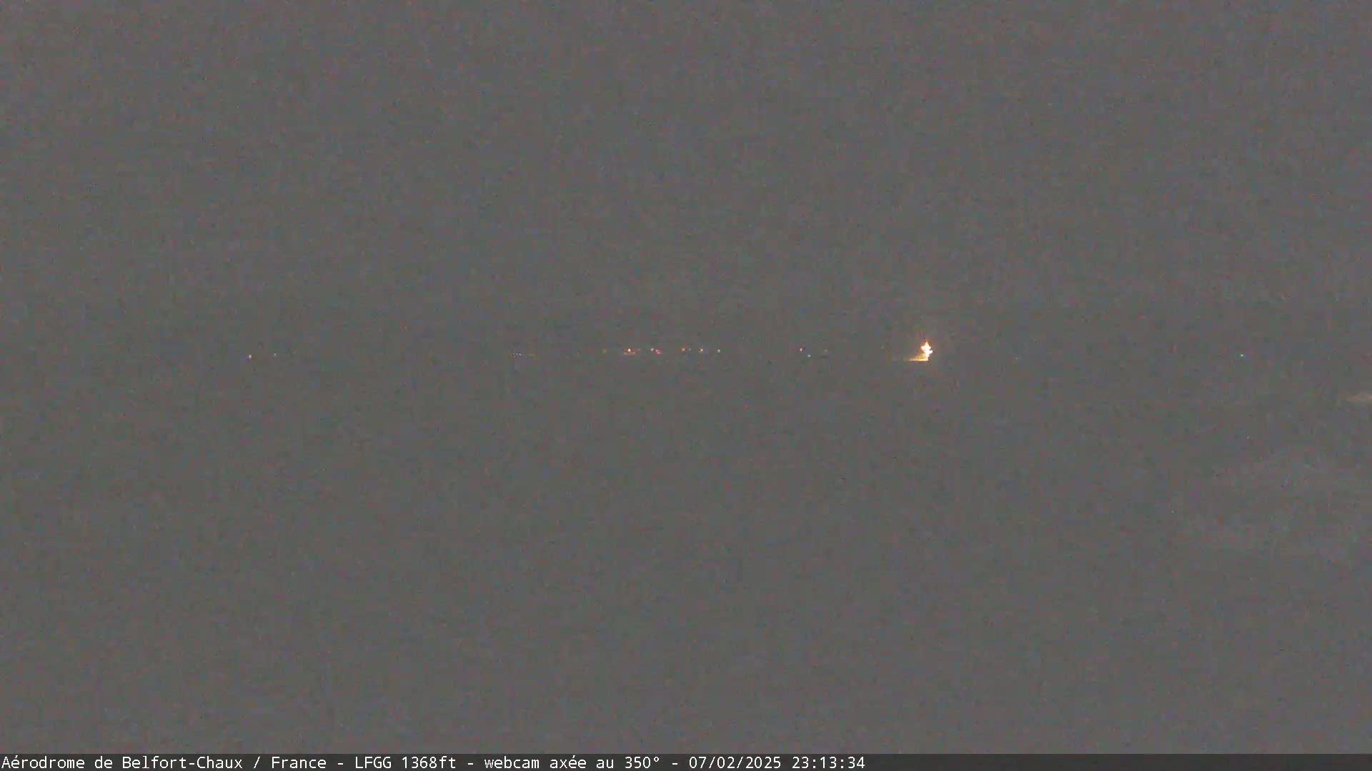A dark, nighttime scene shows a faint line of lights in the distance under a mostly clear sky.