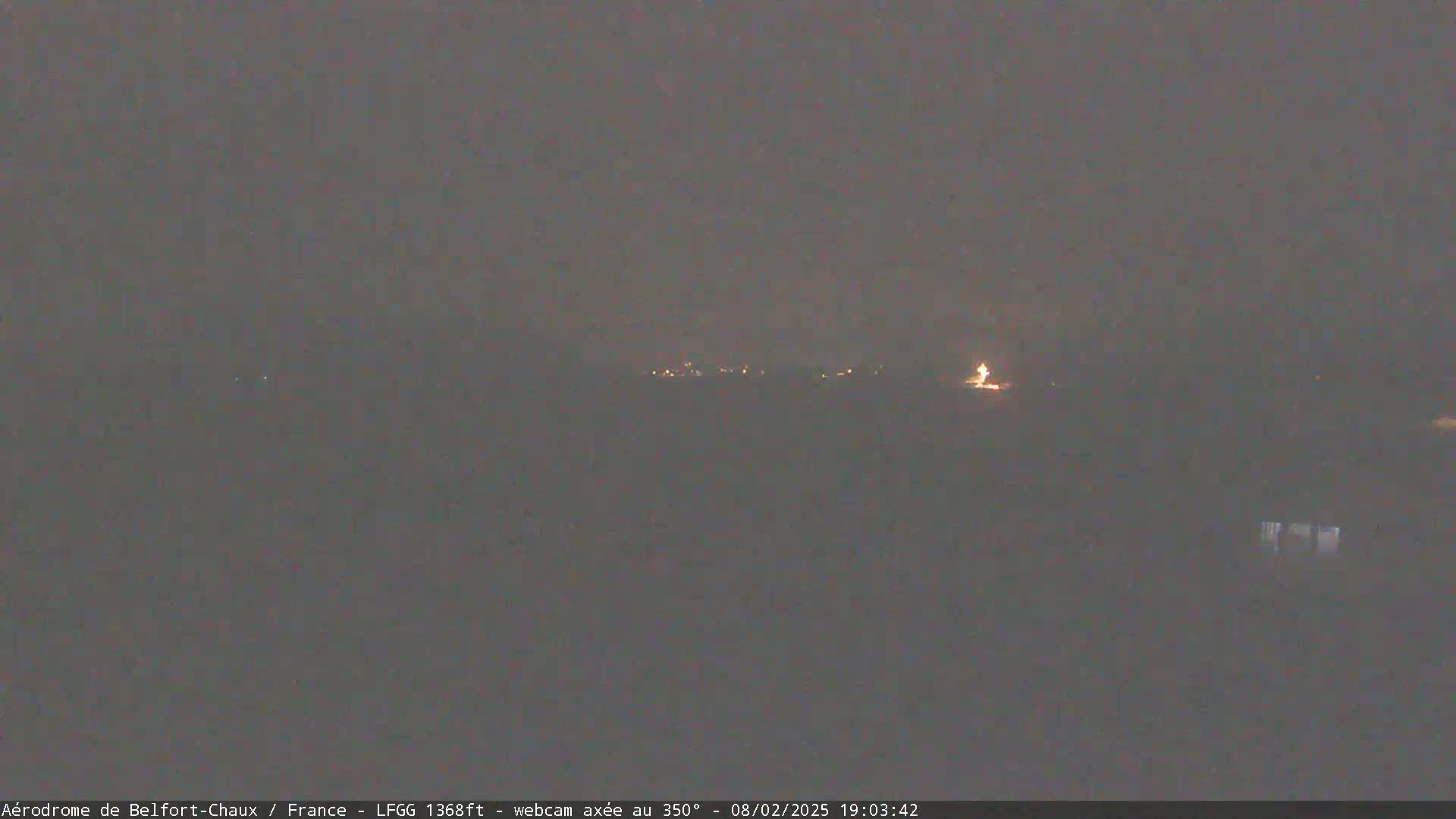 A dimly lit, nighttime landscape is visible, showing a few faint lights in the distance under a dark, overcast sky.