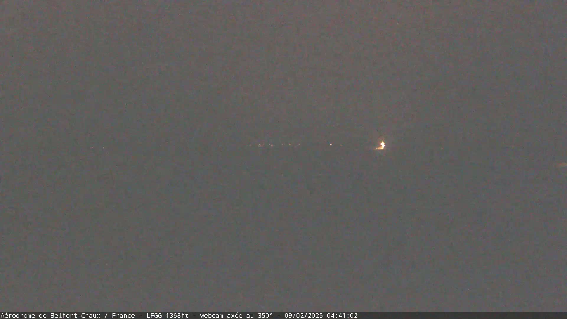 A dark, nighttime scene shows a line of distant lights under a gray sky.