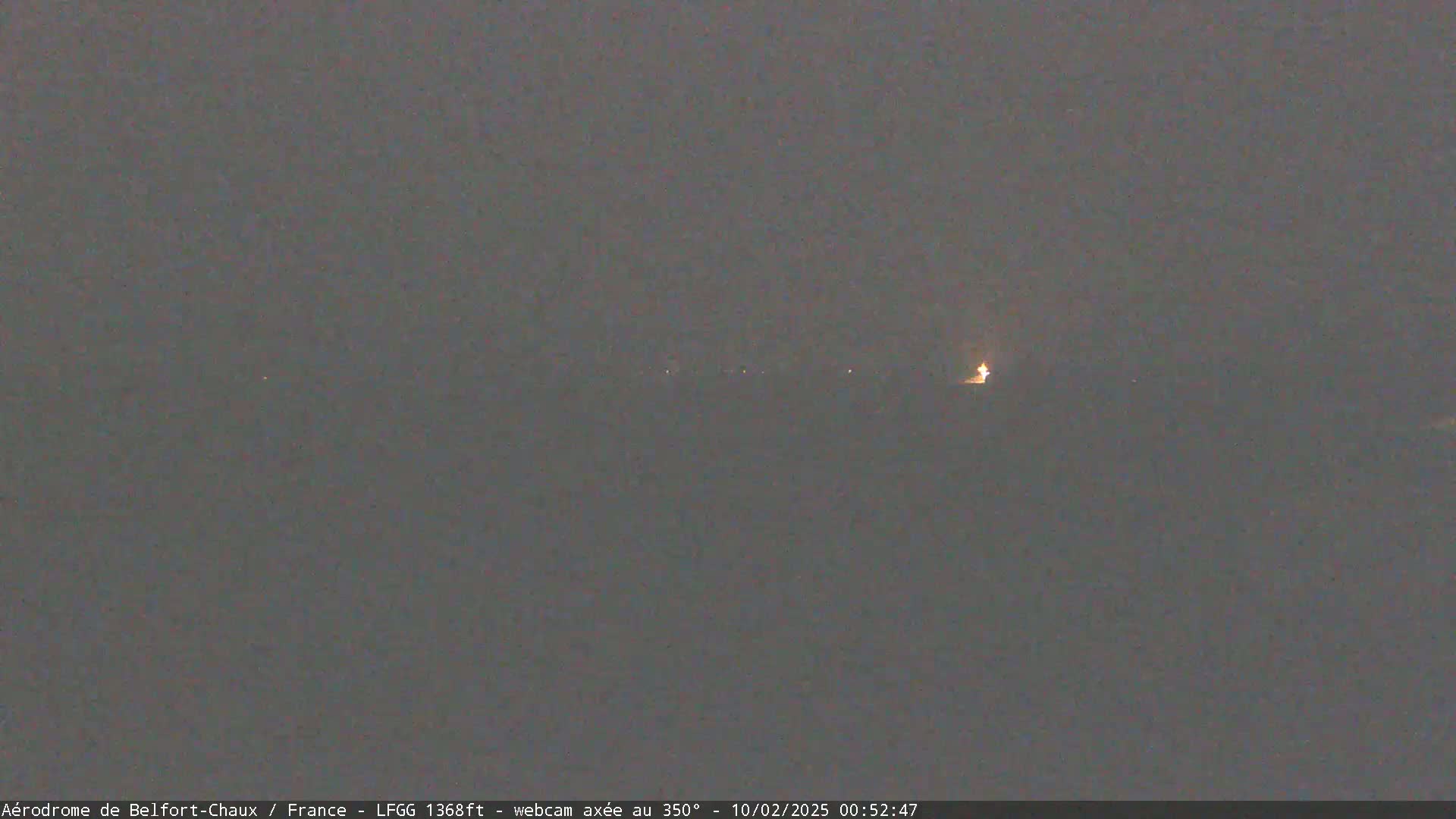 A dark, nighttime scene shows a few distant lights on a flat landscape under a gray sky.