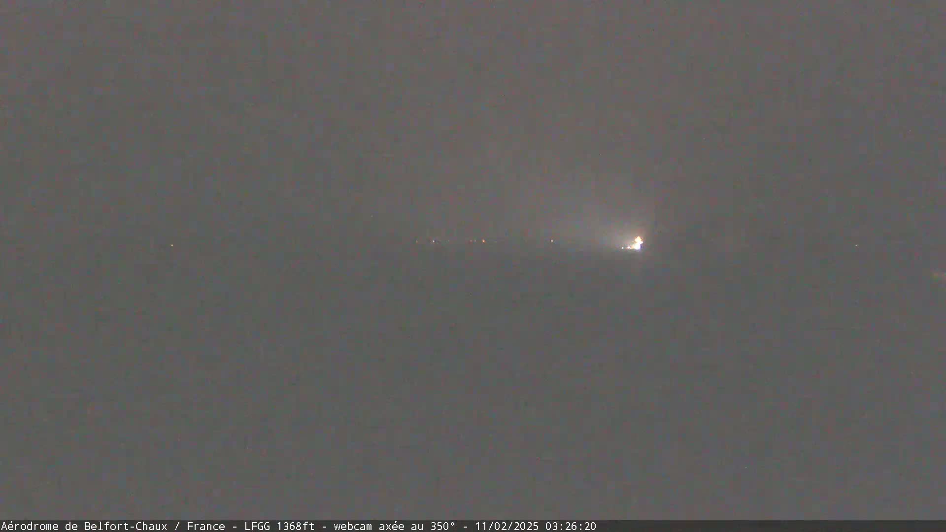 A hazy, dark nighttime scene shows a few faint lights in the distance.