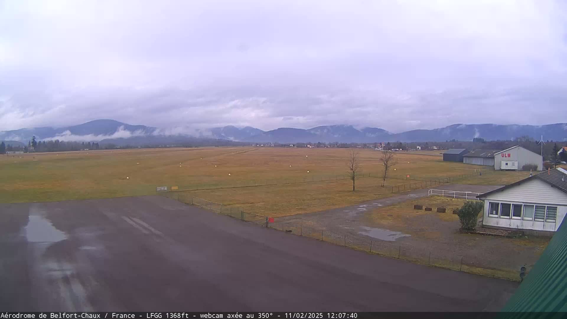 A runway at a small airport stretches towards distant, fog-shrouded mountains under a cloudy sky.