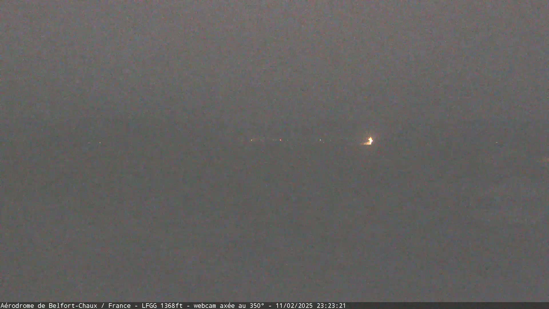 A dimly lit, hazy scene at night shows a few faint lights in the distance.