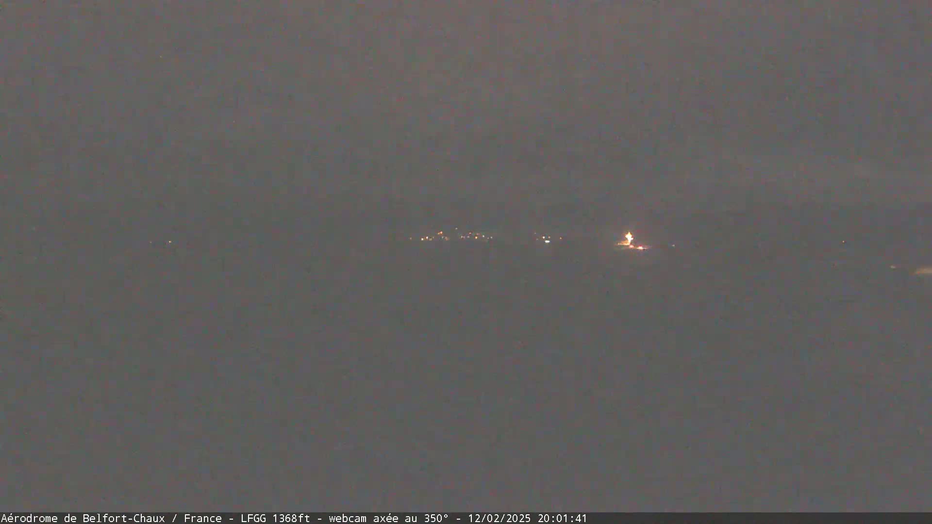 A dark, nighttime view of dimly lit buildings in the distance under an overcast sky.
