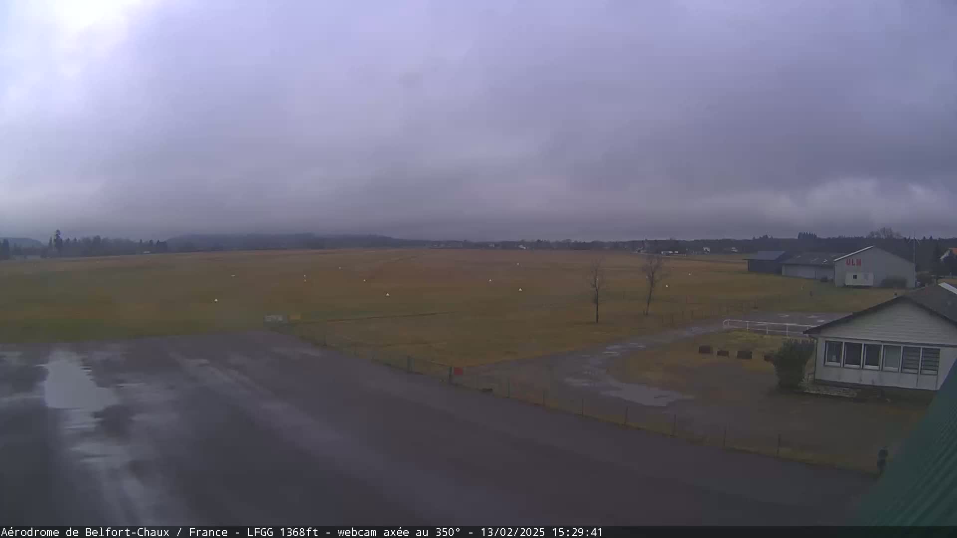 A wet airfield with a few buildings is visible under an overcast sky.